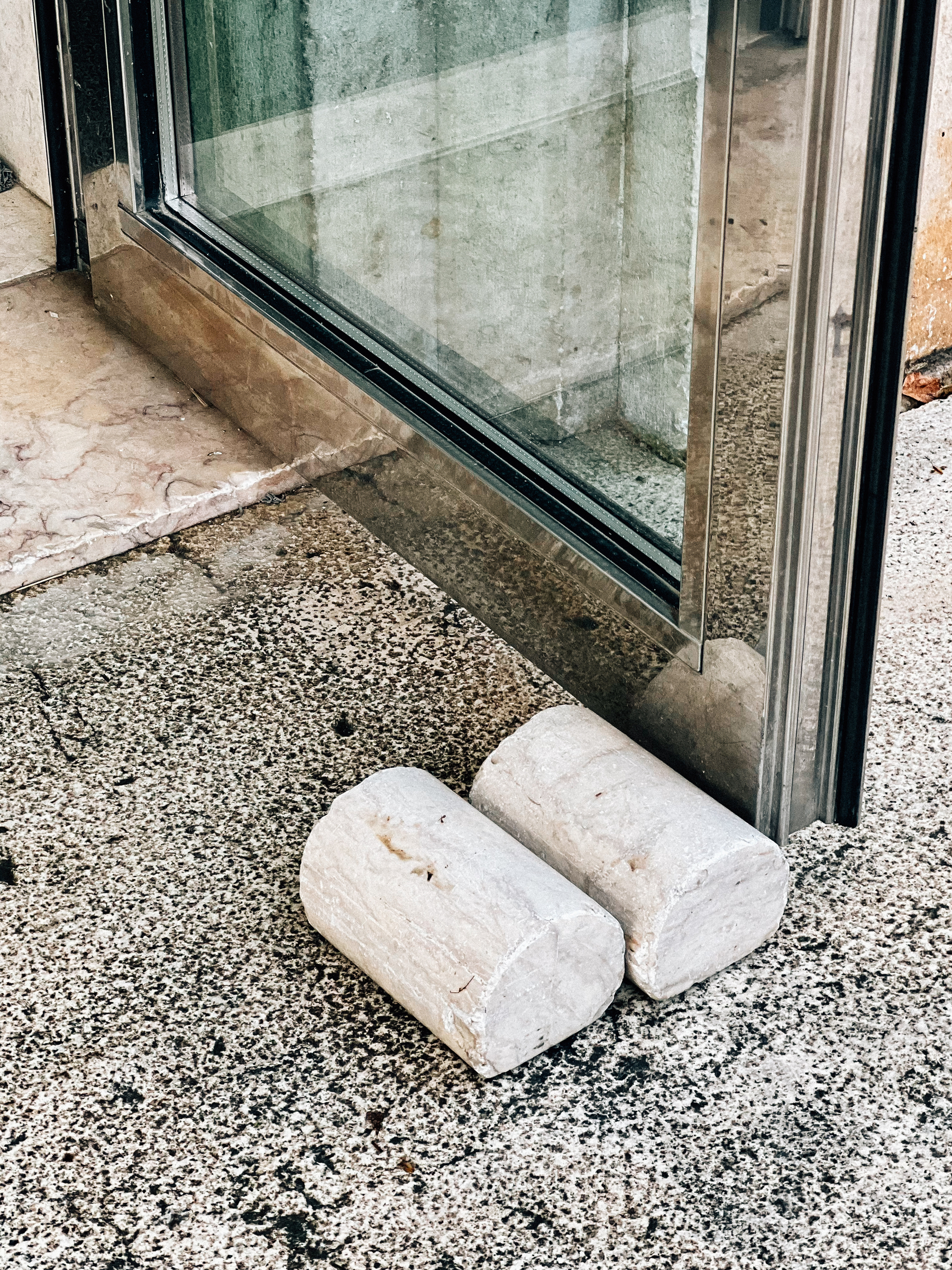 Two stone doorstops placed in front of a glass door on a speckled floor surface.
