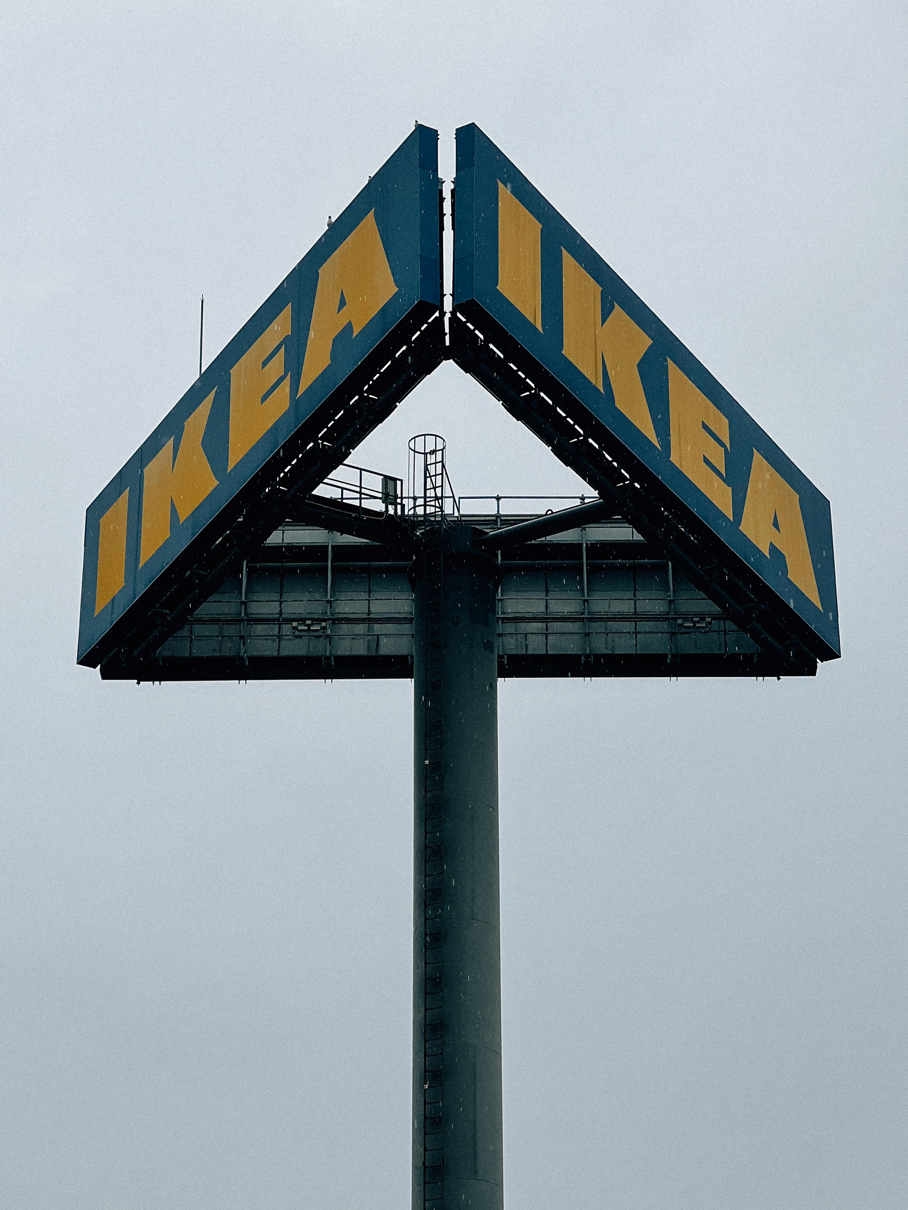 Large IKEA sign on a post against a cloudy sky.