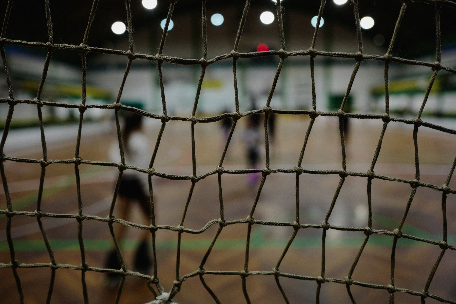 A close-up view of a net with a blurred scene of players on the court in the background.