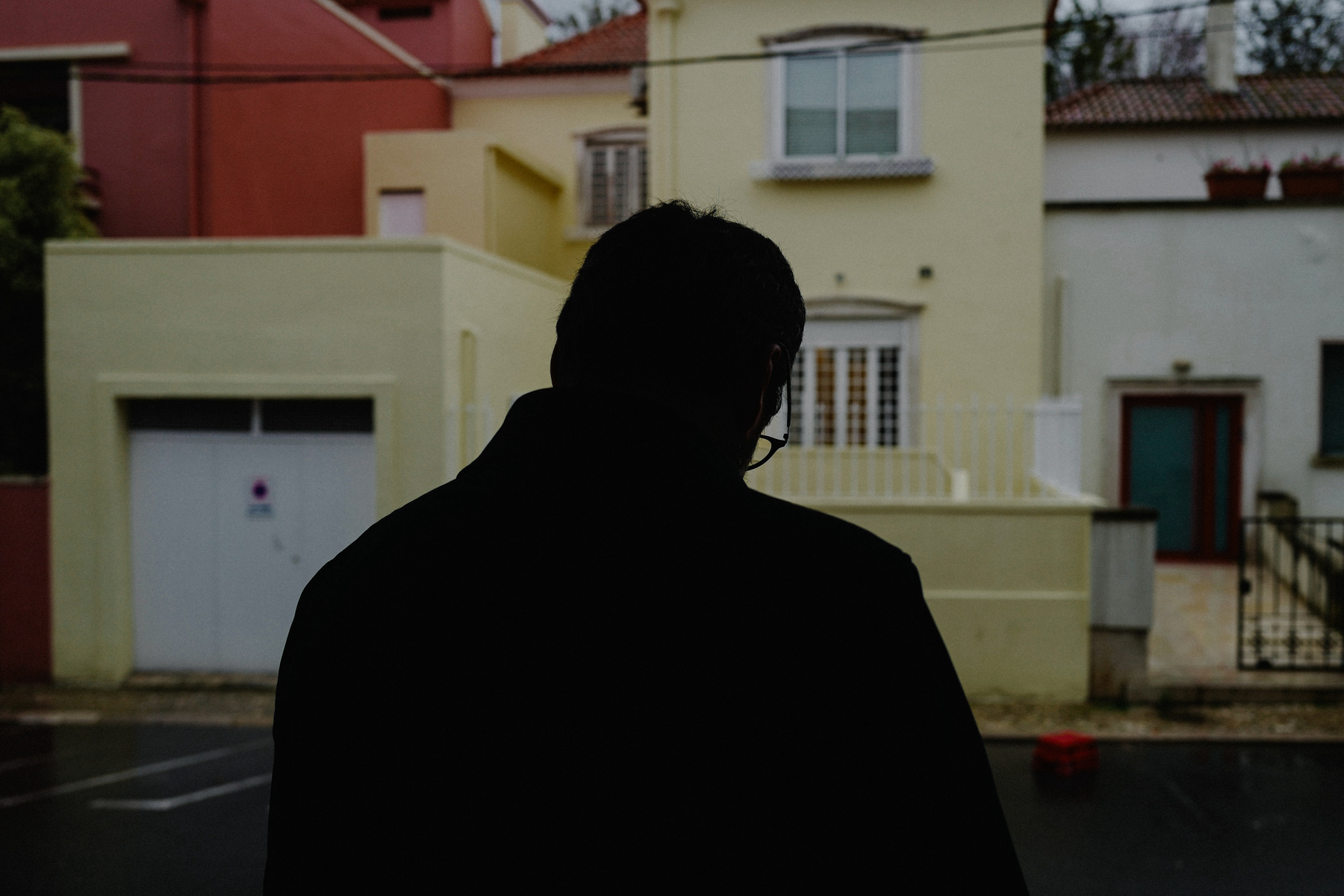 Silhouetted individual facing away from the camera, looking at a street lined with colorful buildings, under overcast skies.