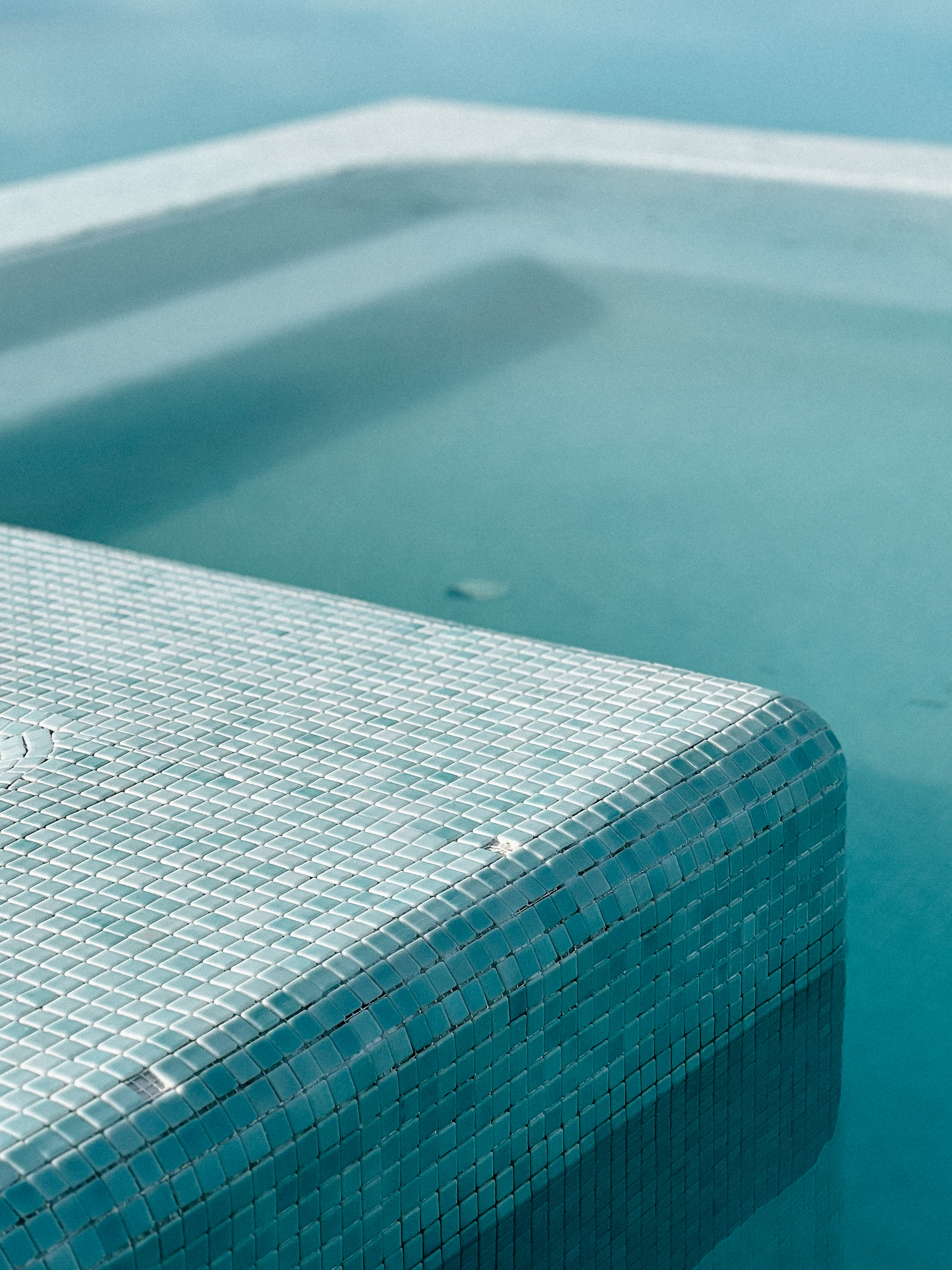 Edge of a swimming pool with clear blue water and a mosaic tile pool deck.