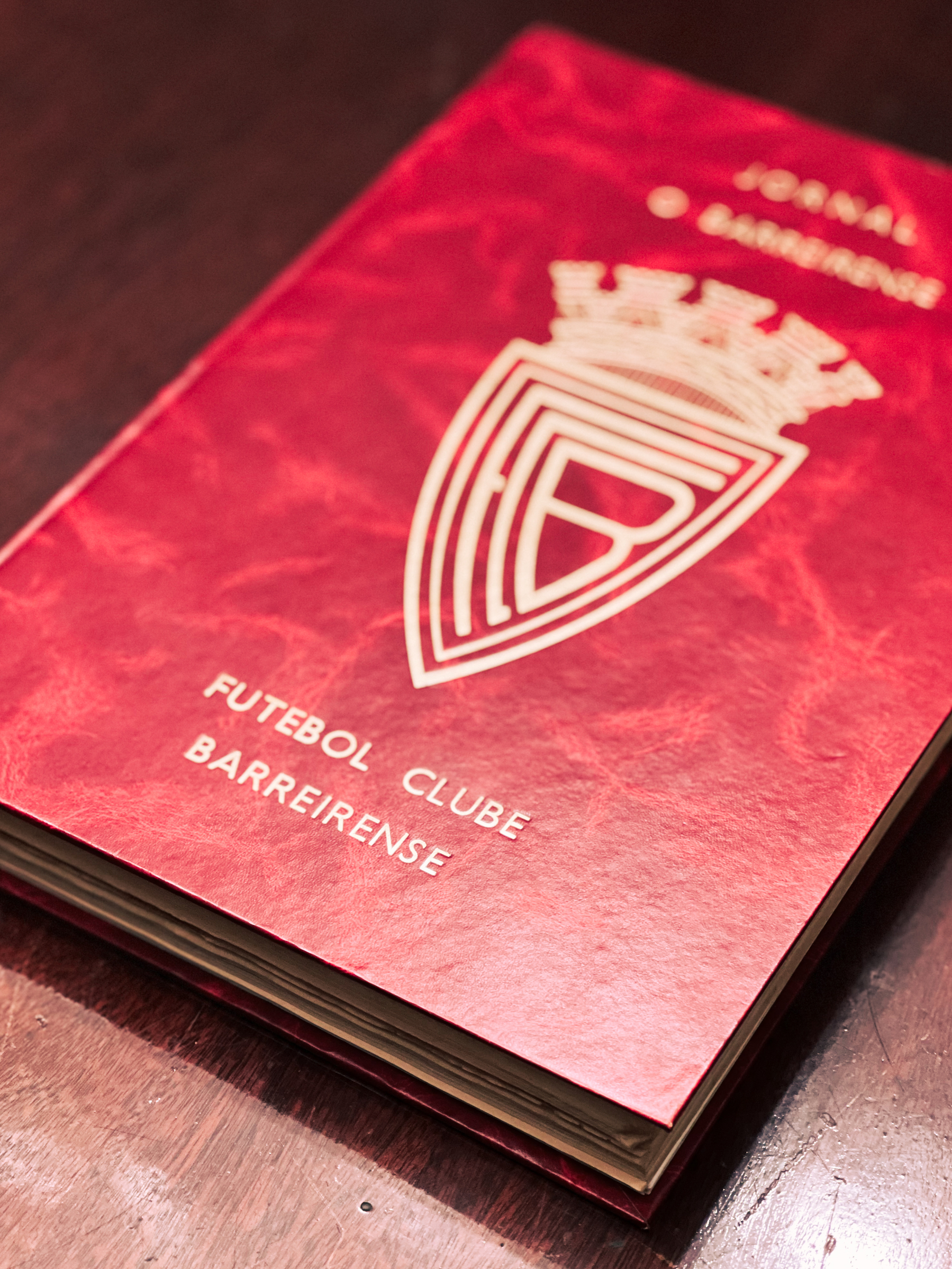 A red book with the emblem and the words &ldquo;Futebol Clube Barreirense&rdquo; on the cover, placed on a wooden surface.