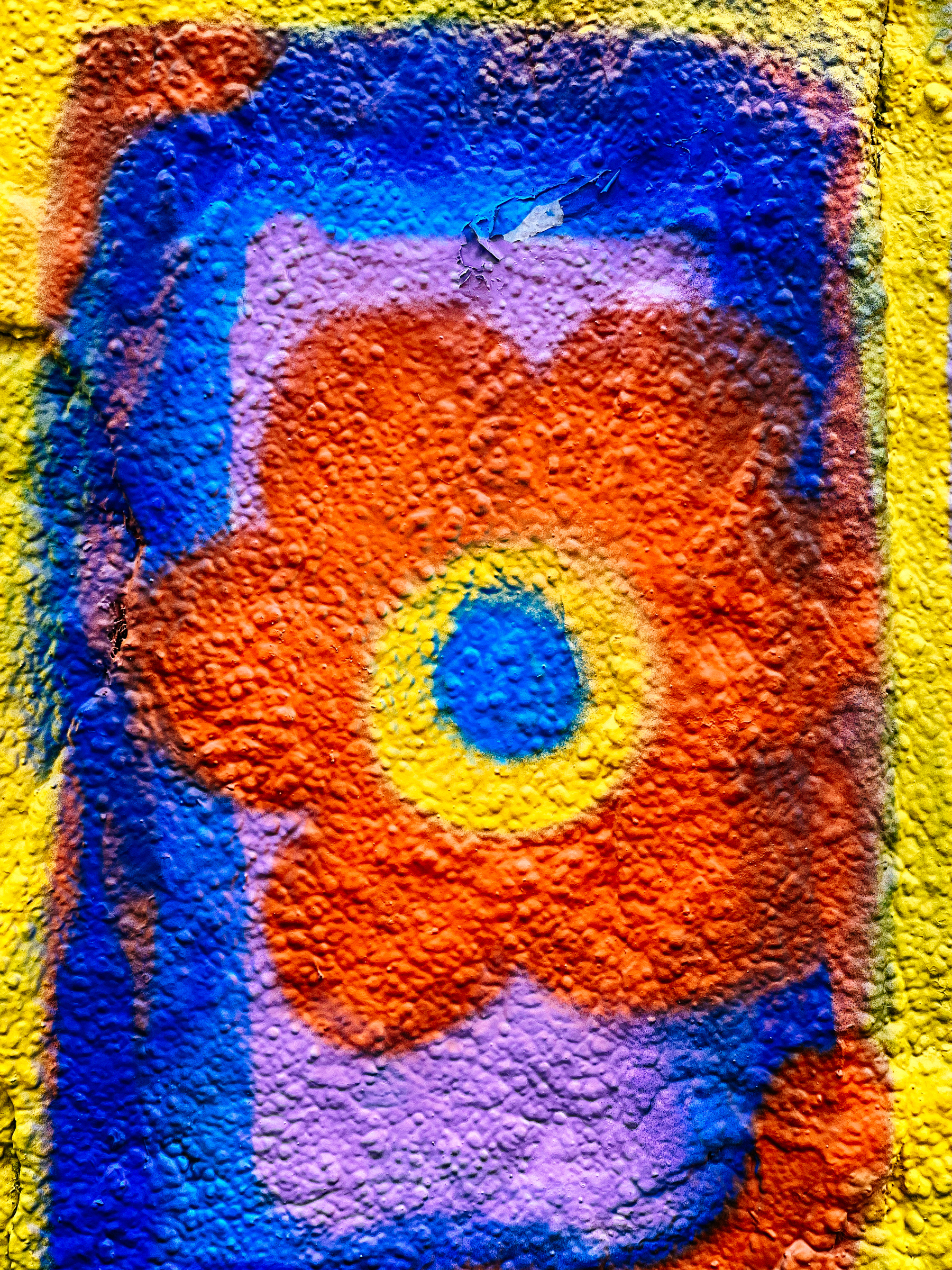 Graffiti of a colorful abstract flower with a blue center, orange petals, and a purple outline on a textured wall with yellow and blue background.