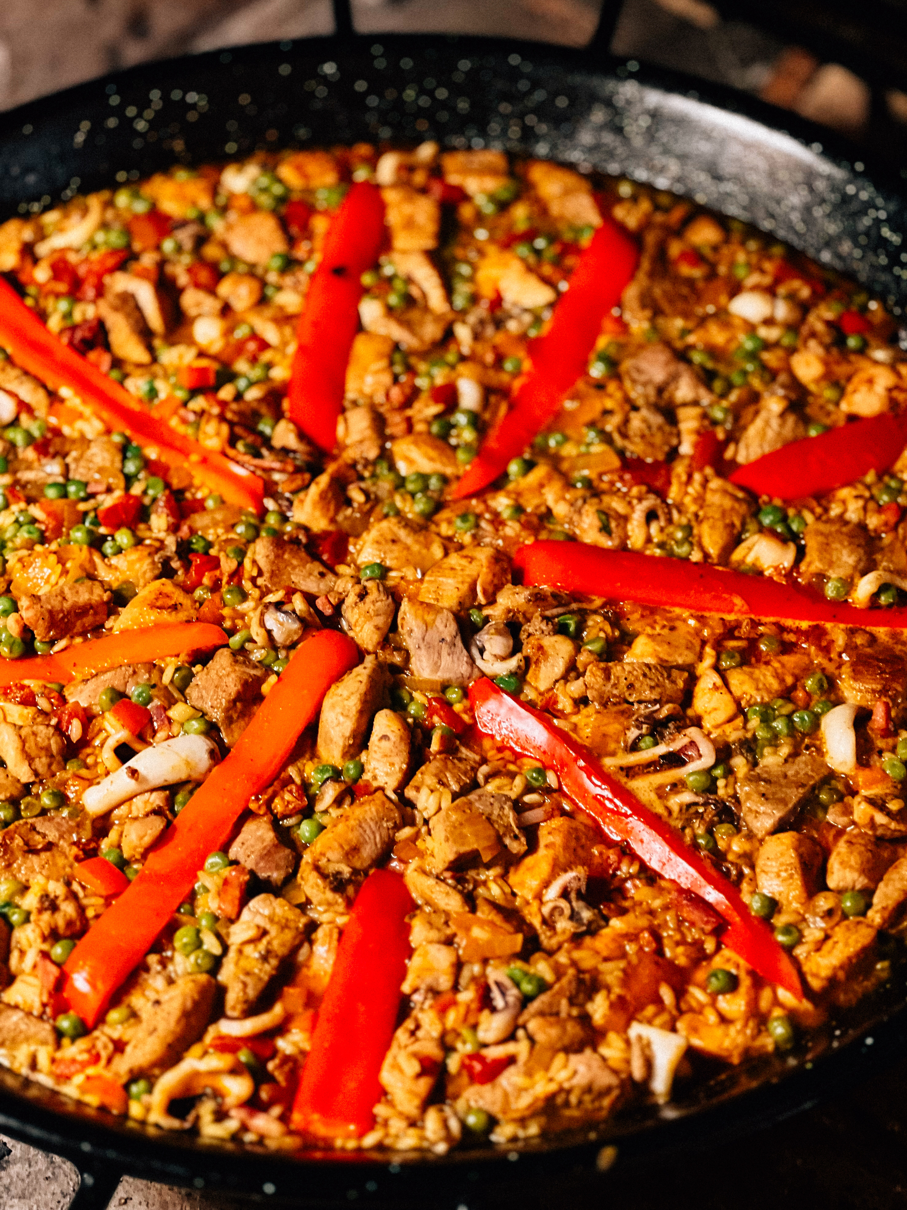 Paella with chicken, red bell peppers, peas, onions, and rice in a paella pan.