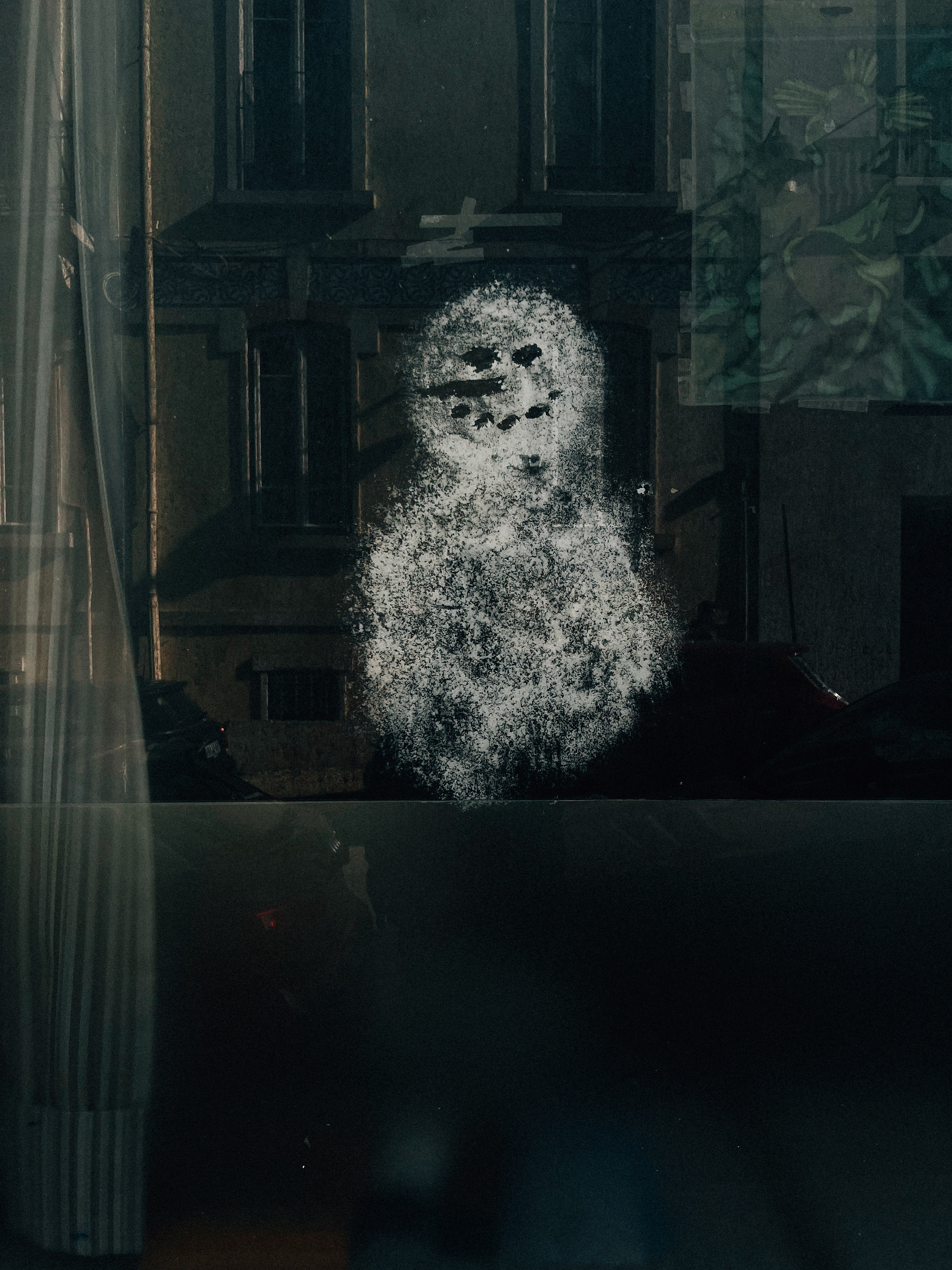 A mysterious silhouette of a snowman appears on a glass pane, with the reflection of a building and parked cars in the background.