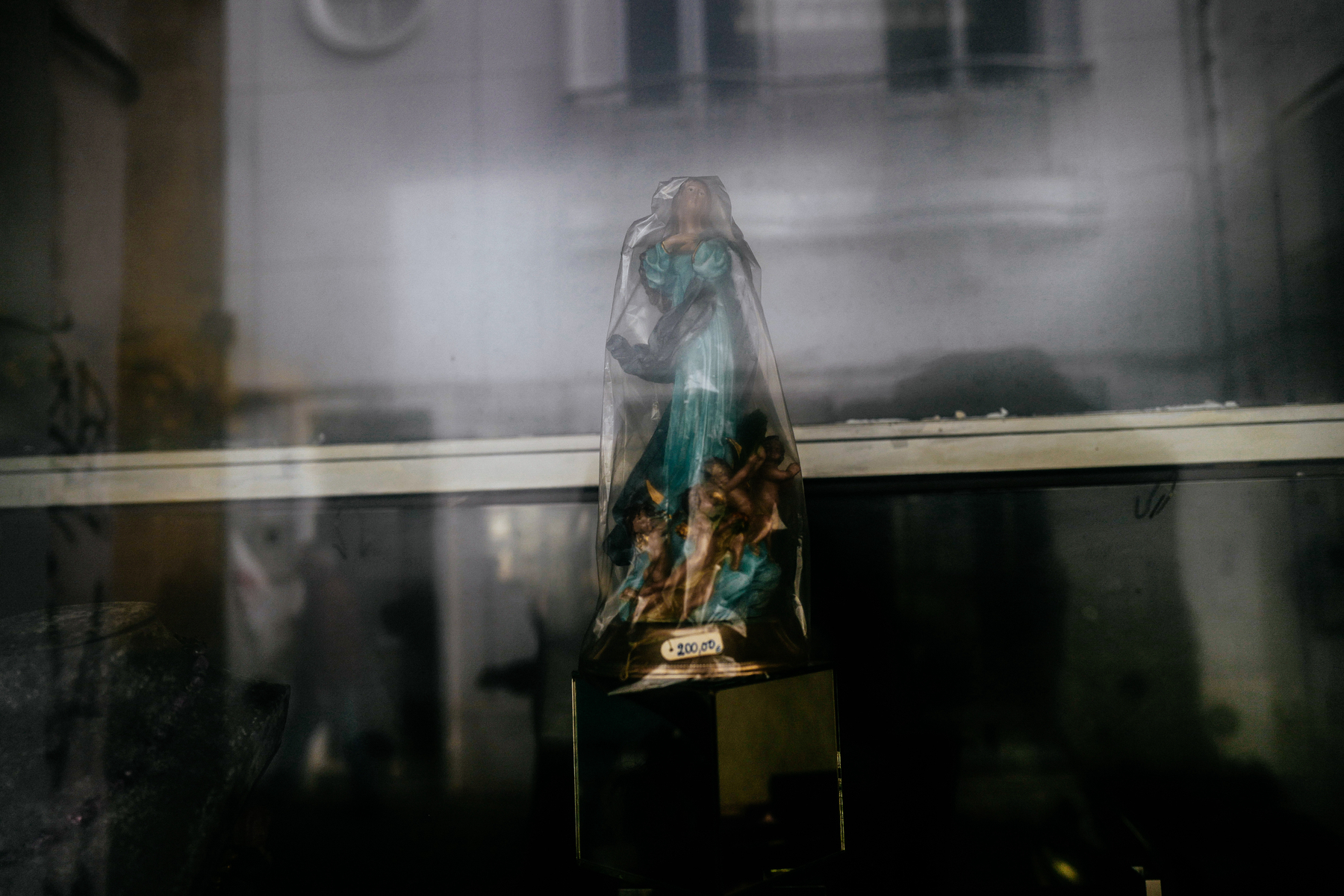 A statue of the Virgin Mary wrapped in plastic, displayed behind a glass window with a €200.00 price tag.
