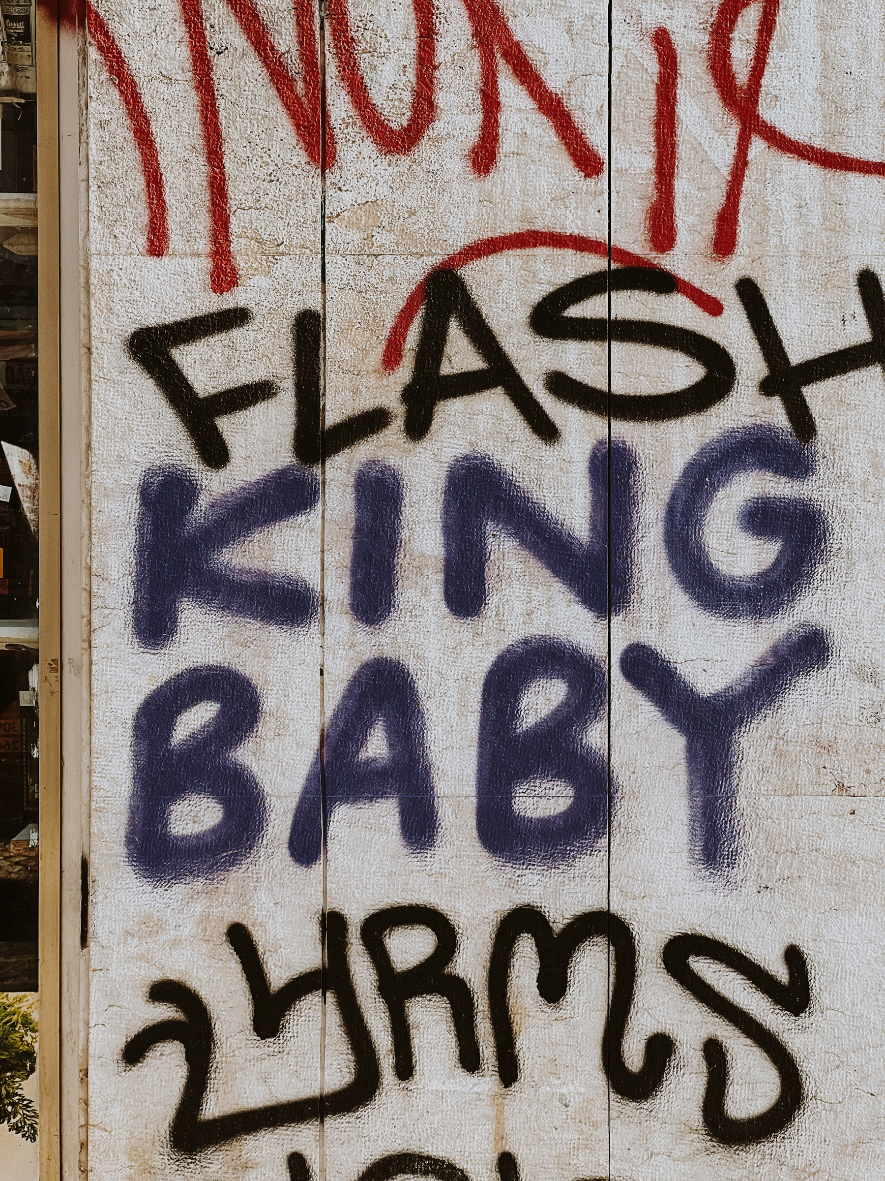 Graffiti on a wall with the words &ldquo;FLASH KING BABY&rdquo; in black and purple spray paint over a white background.