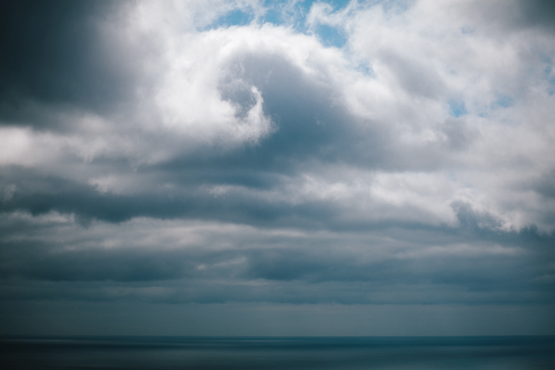 A serene seascape under a dramatic sky with various cloud formations, extending from fluffy white to ominous grey.