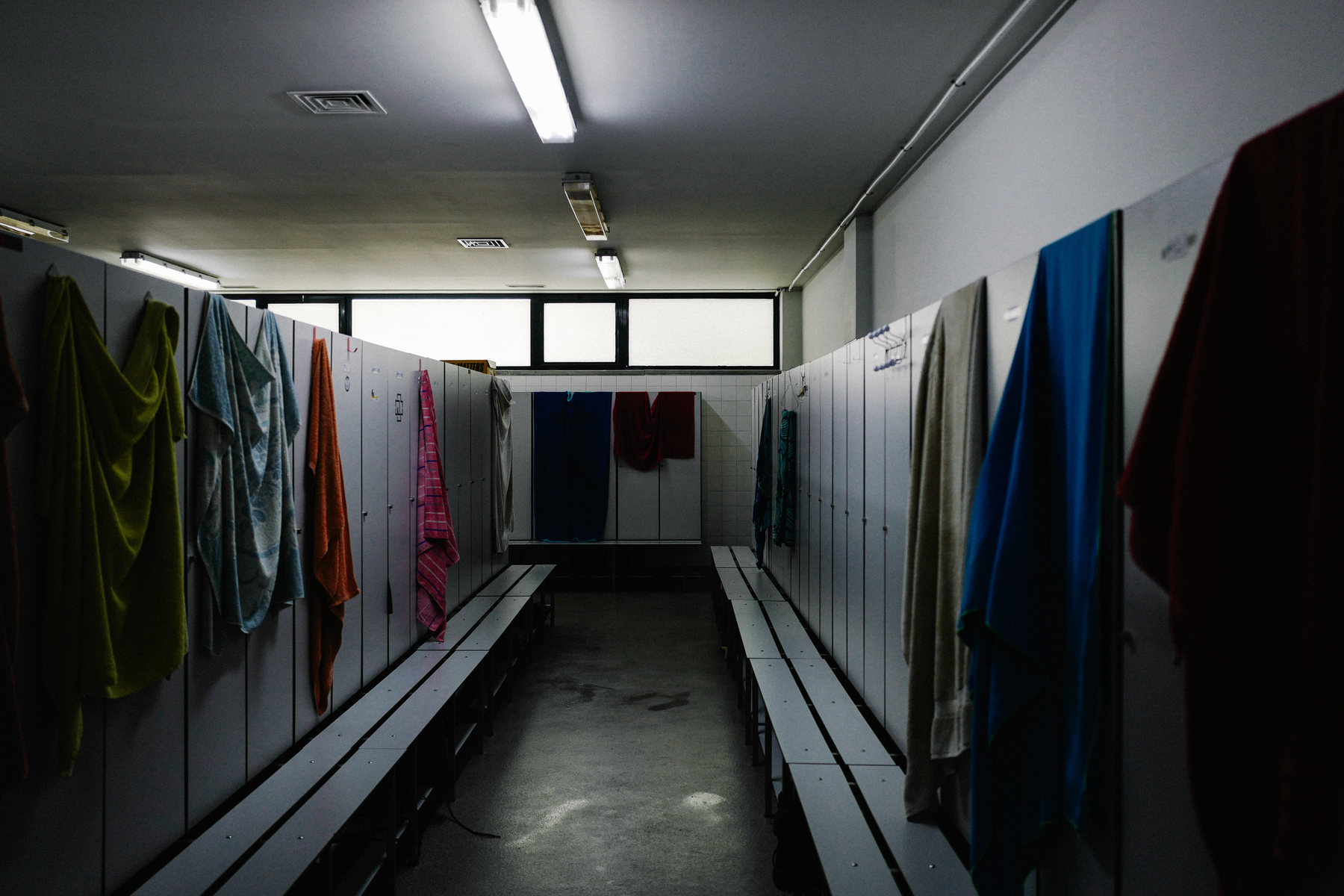 A dimly lit changing room with benches and lockers, towels hanging from the partitions and the bench.