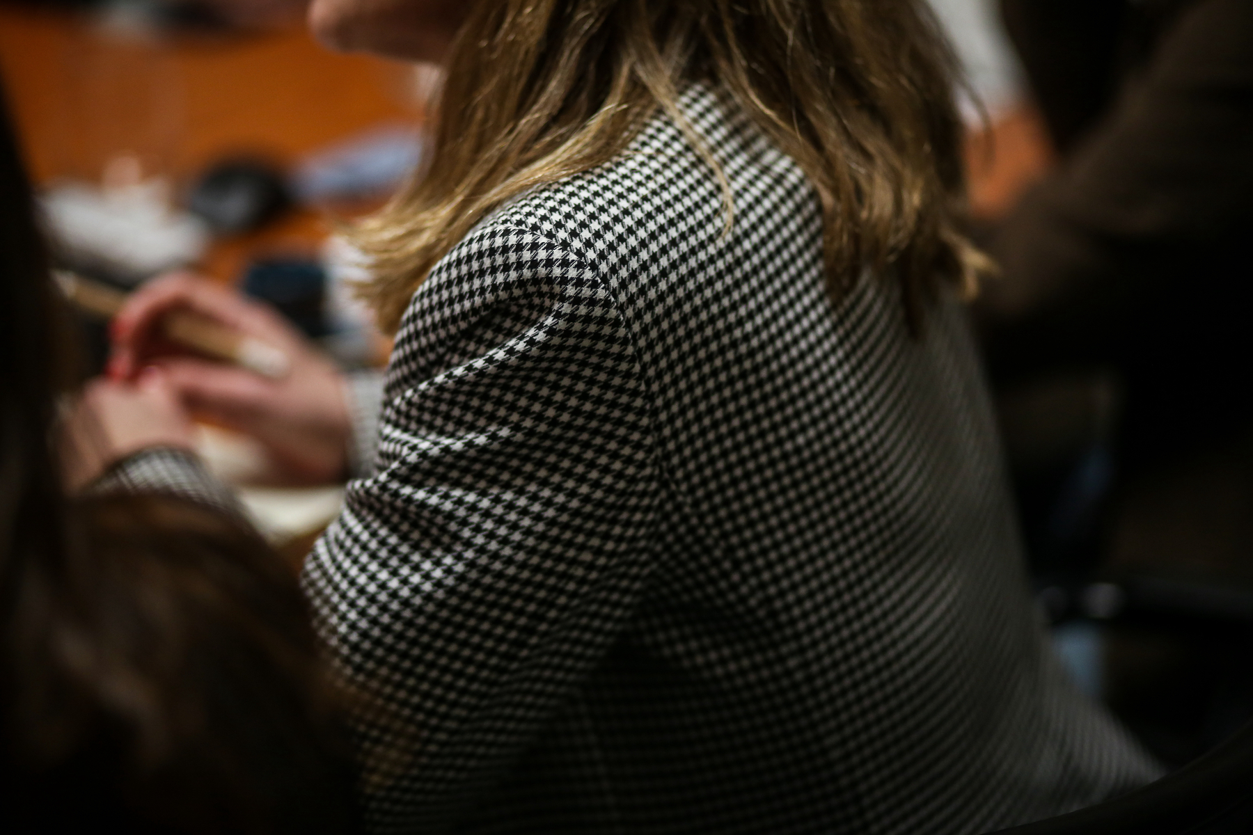 A person from behind wearing a pied de poule patterned blazer, slightly out of focus, with their hair covering part of the collar.