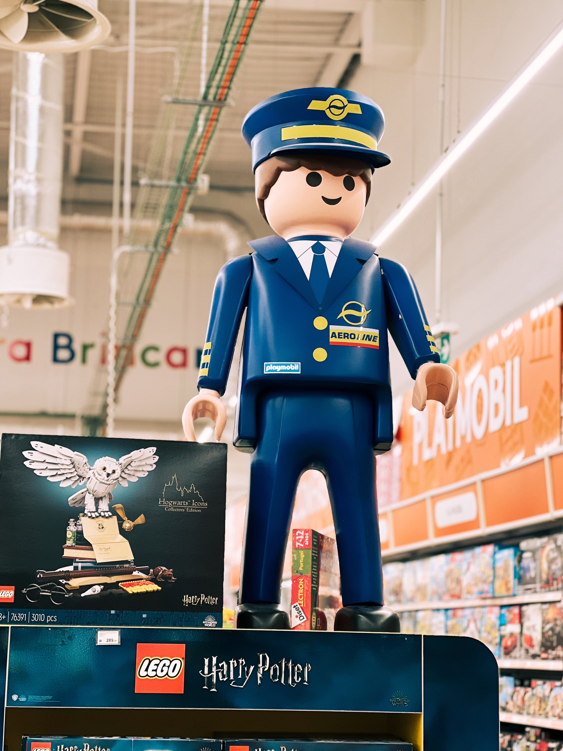 A large Playmobil figure resembling a pilot in a blue uniform, standing atop a Harry Potter LEGO set display shelf in a store.