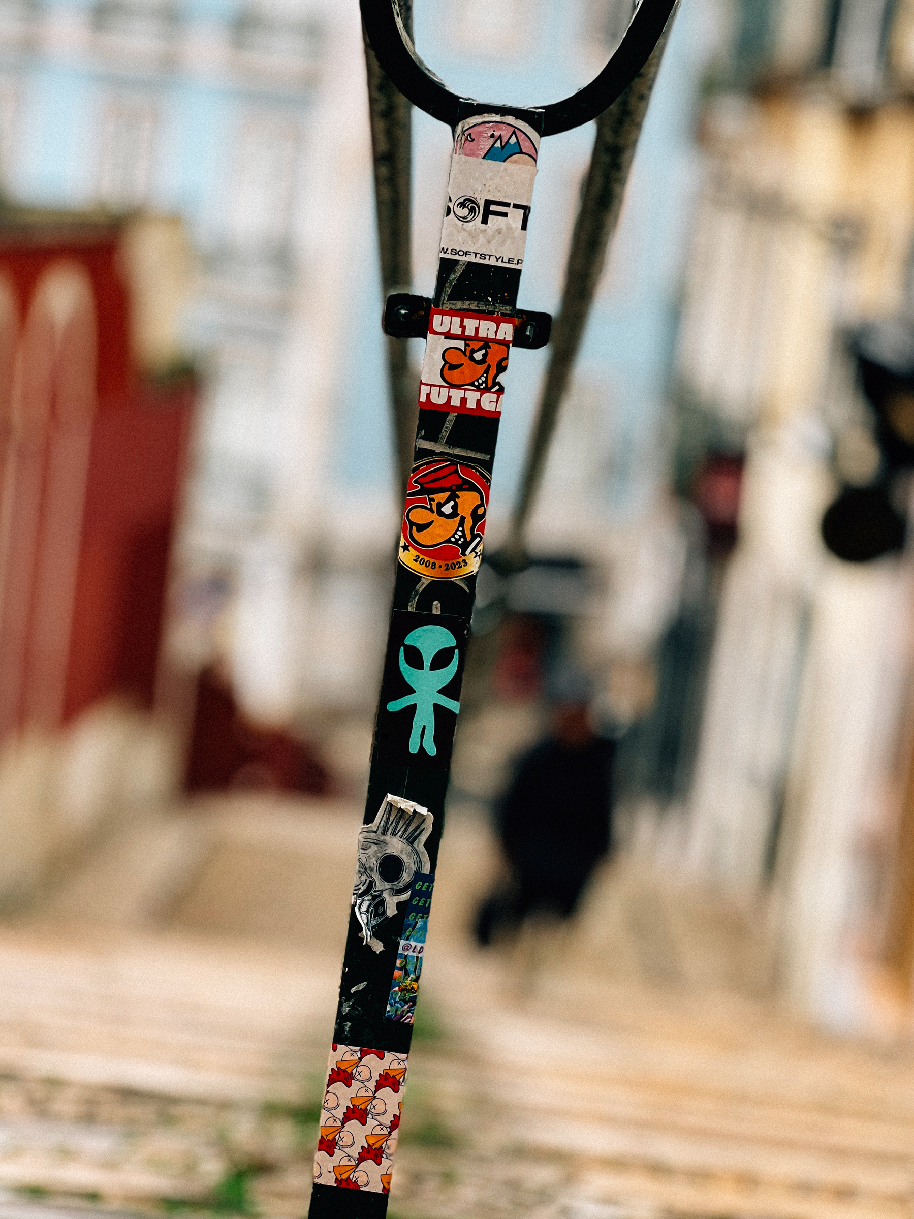 A close-up of a street pole covered in various stickers, with a blurred urban background.