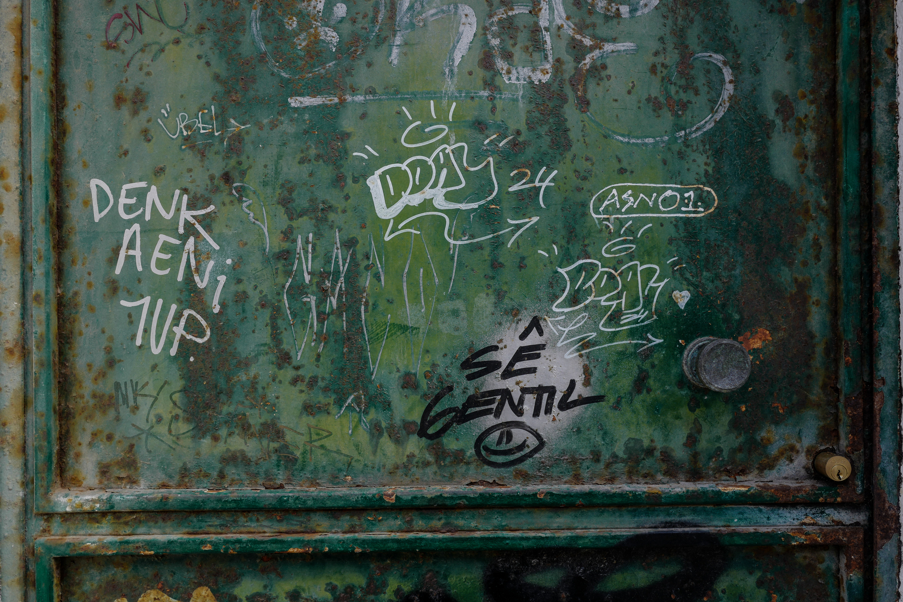 Graffiti tags and scribbles on a weathered and rusting metal surface.