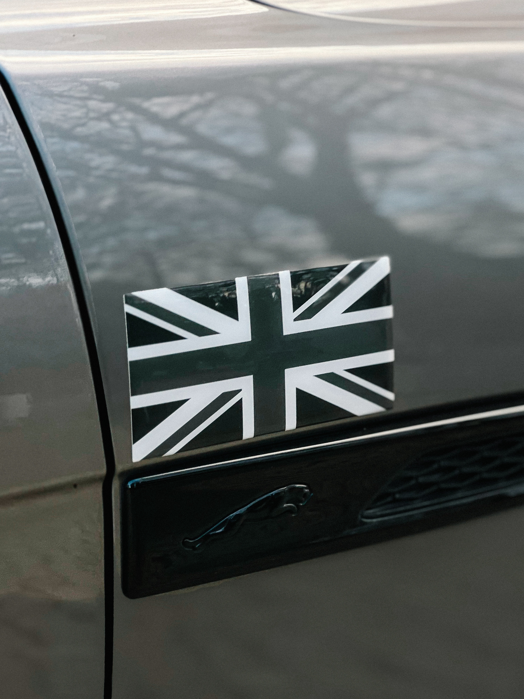 Black and white Union Jack flag sticker on a car&rsquo;s body, close up shot with focus on the flag, car&rsquo;s color and sticker details visible. Jaguar beneath the sticker.