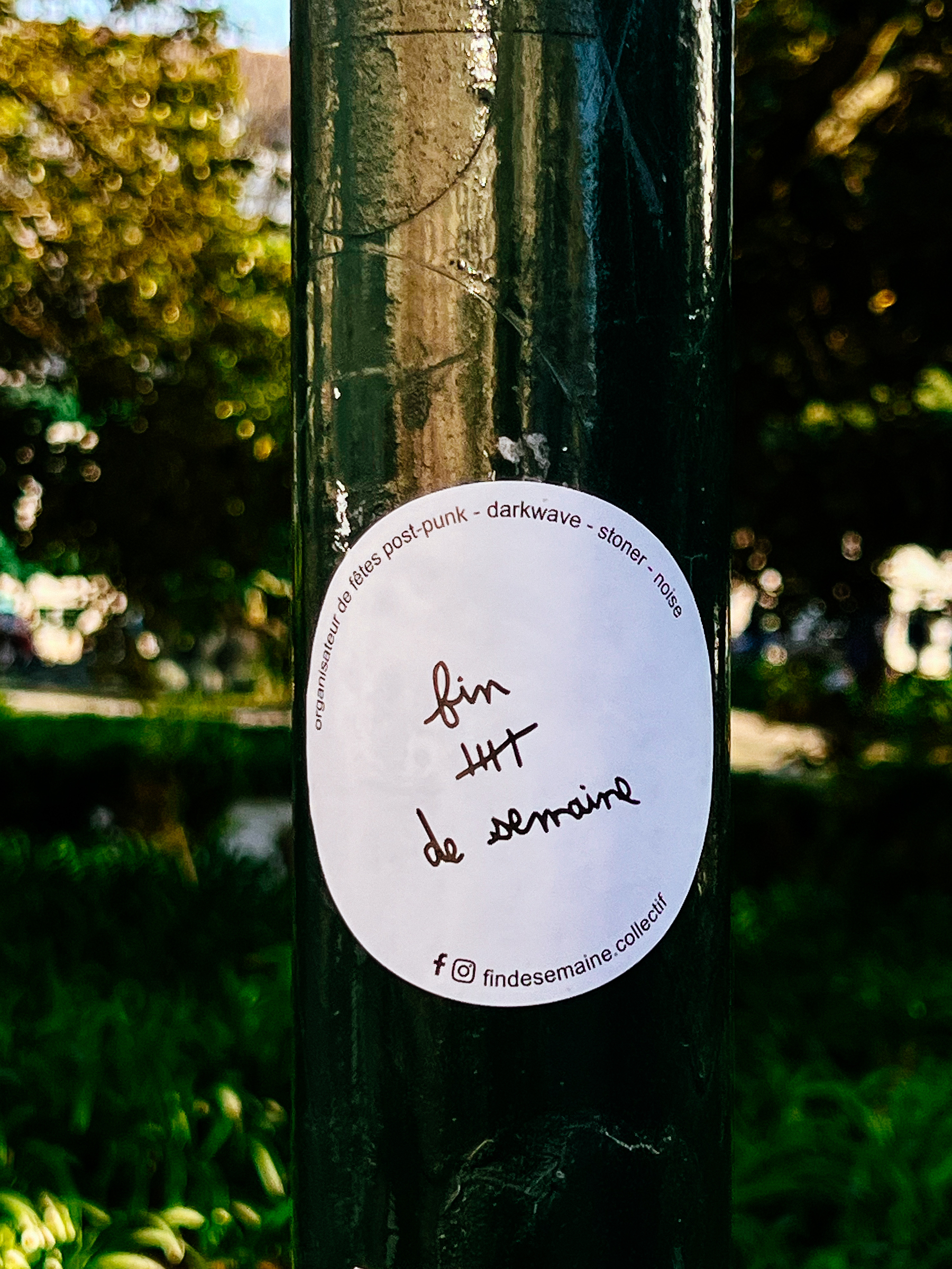 A sticker on a pole, with handwritten text &ldquo;fin de semaine&rdquo;. Backdrop of blurred greenery.