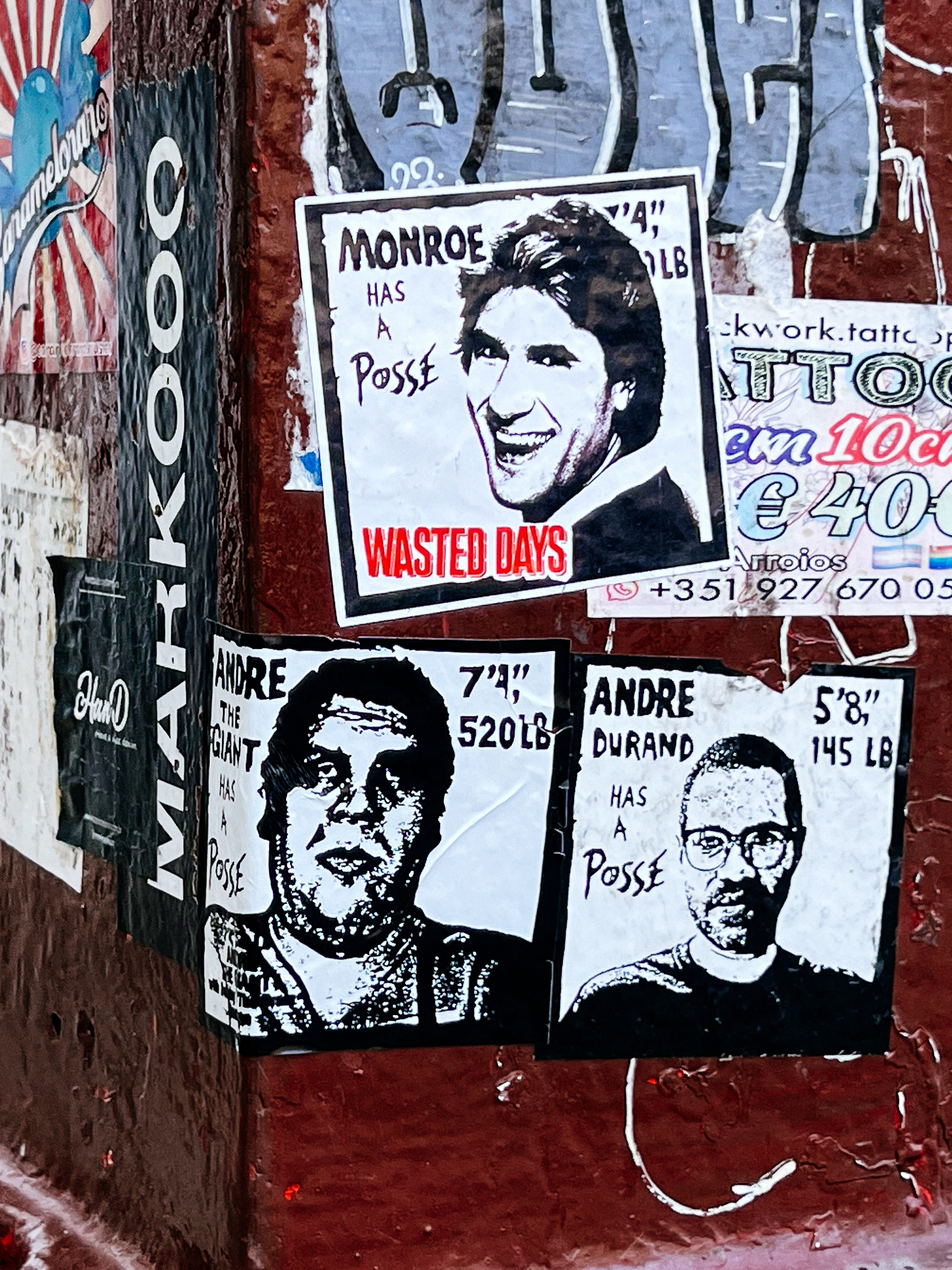 Stickers on a wall show stylized portraits with text: &ldquo;MONROE HAS A POSSE WASTED DAYS,&rdquo; &ldquo;ANDRE THE GIANT HAS A POSSE,&rdquo; and &ldquo;ANDRE DURAND HAS A POSSE.&quot;