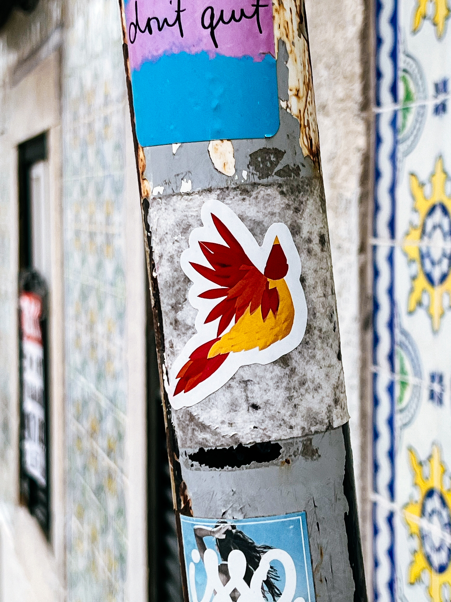 Stickers on a pole, one with a winged design and another saying &ldquo;don&rsquo;t quit,&rdquo; next to decorative tiles.