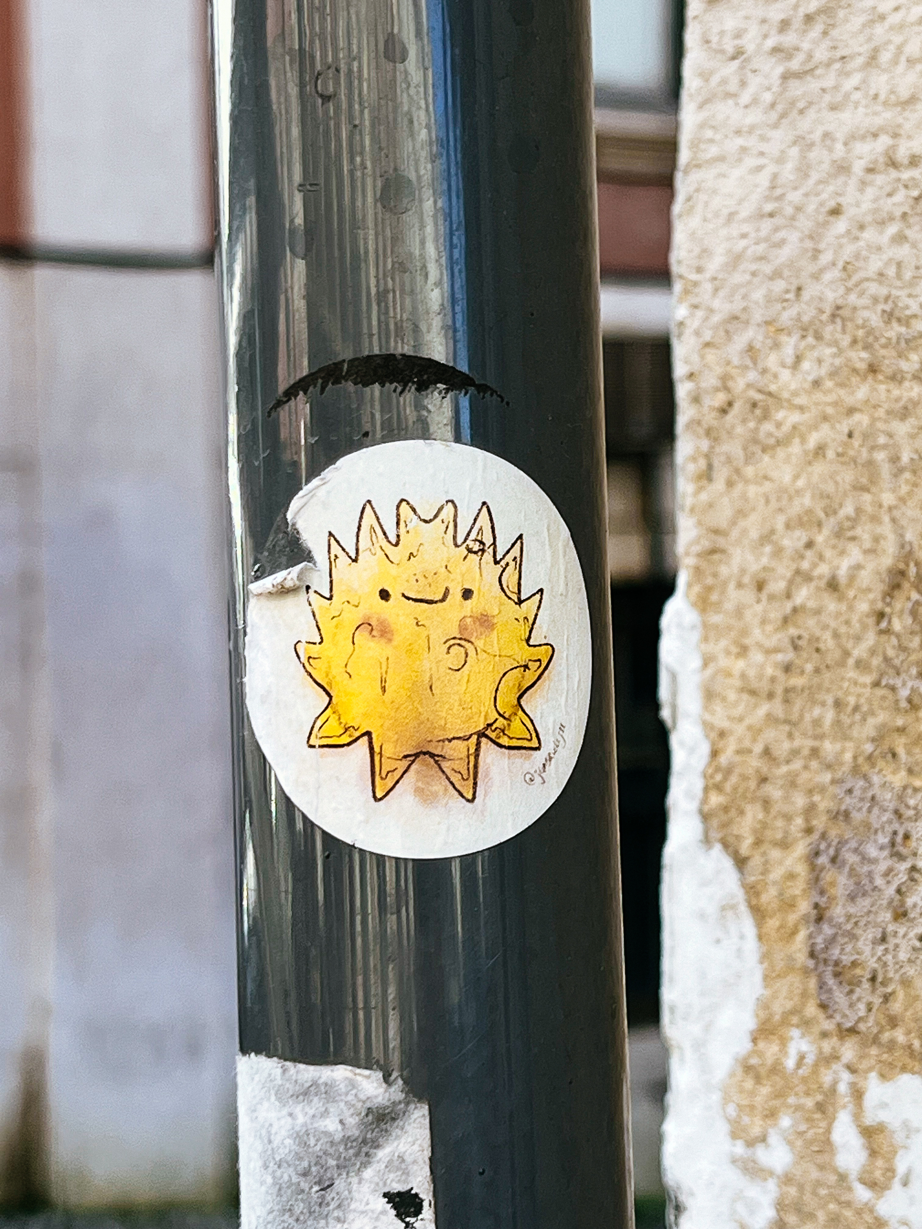 A weathered sticker depicting a smiling sun is affixed to a metal pole, flanked by rough wall textures.