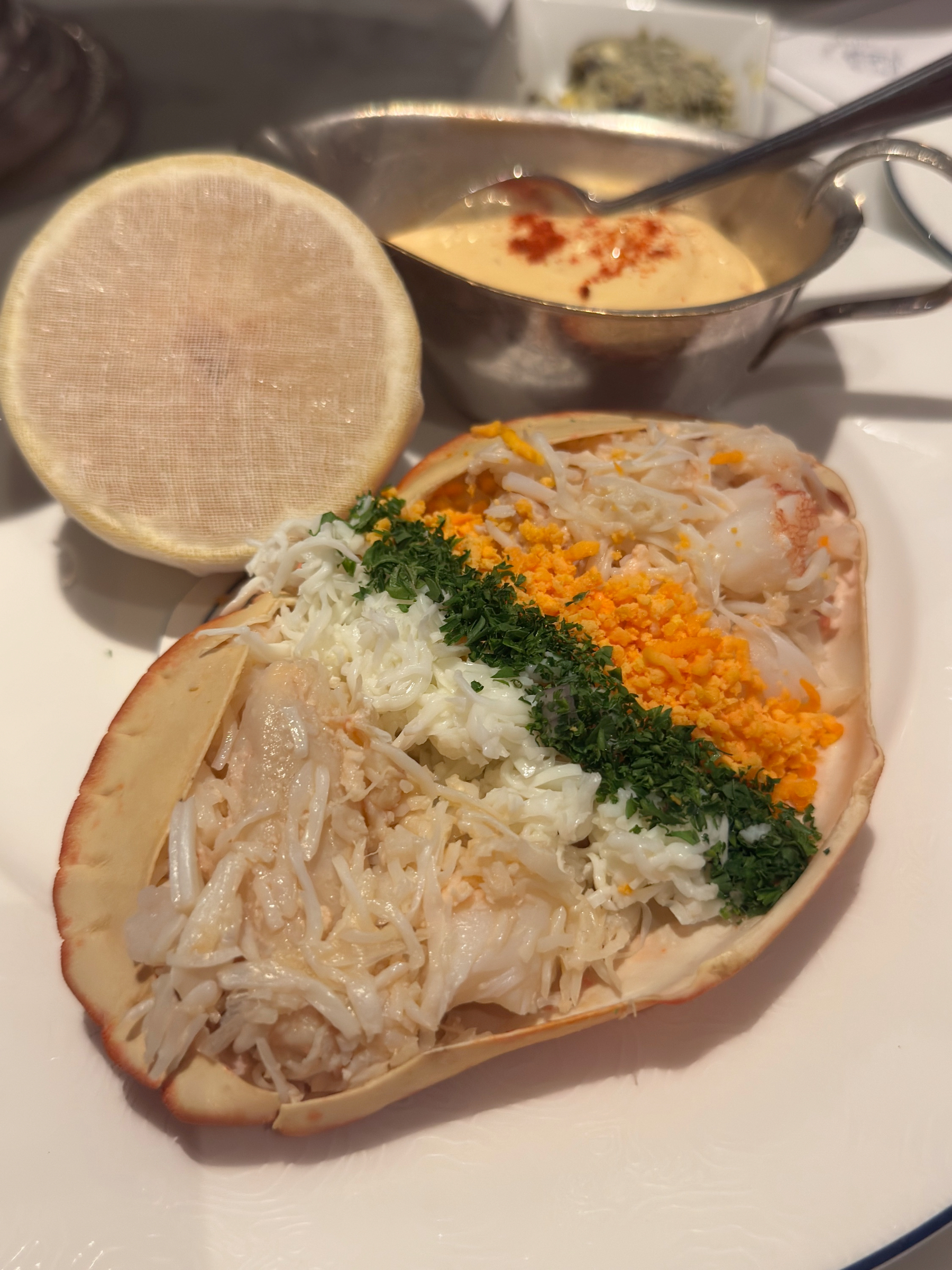 A dressed crab presented in its shell, generously filled with sweet white and brown crab meat and neatly topped with chopped herbs and vivid orange roe, with classic sauces and toast on the side.