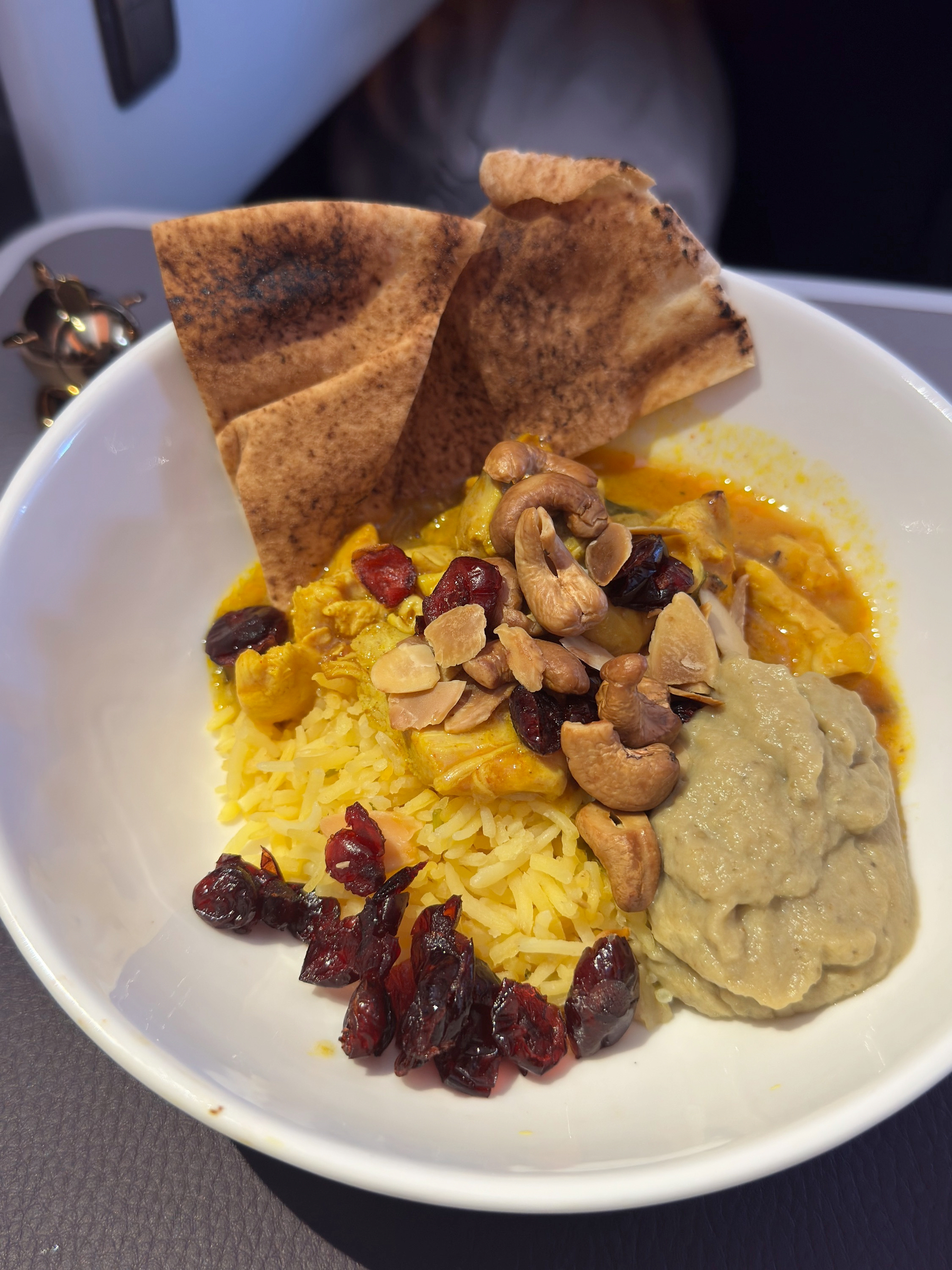 A colorful bowl of fragrant yellow rice topped with spiced curry, toasted cashews, dried cranberries, creamy puree, and crisp flatbread tucked on top.