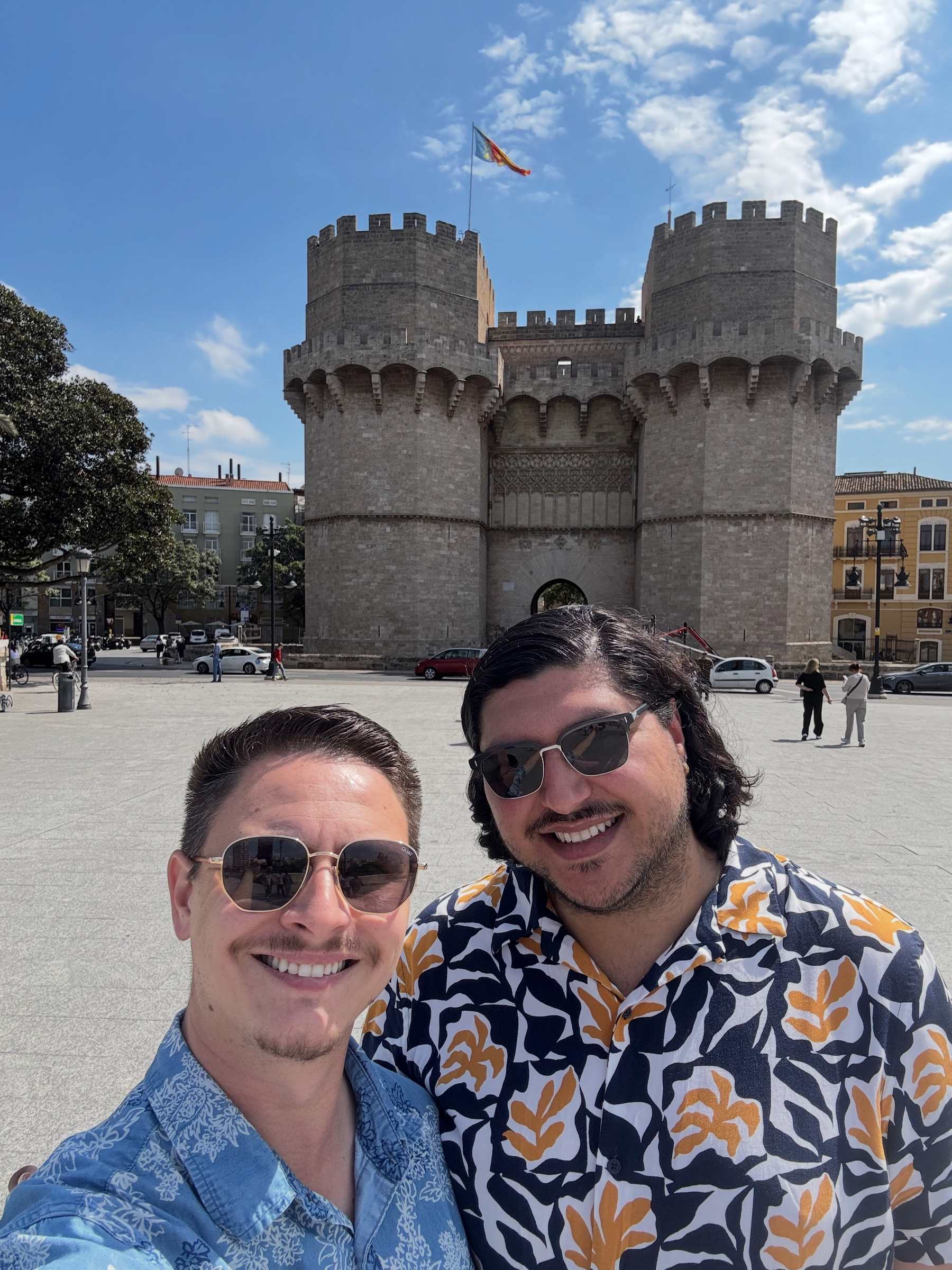 Hugo and I posing in front of the Torres de Serranos, the twin stone towers rising behind us as cars and pedestrians pass through the open city gate.