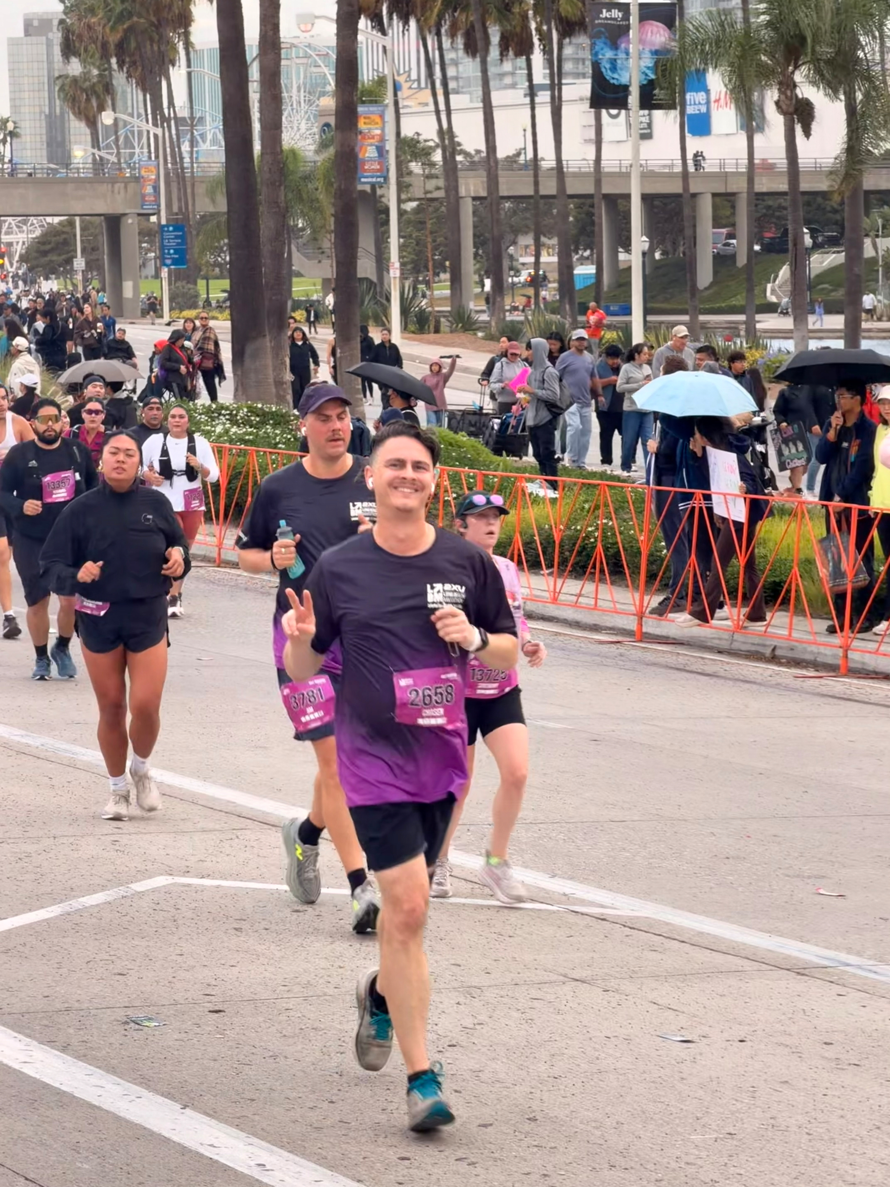 A group of runners (with me in the front) participating in the race on a street lined with palm trees and spectators behind barriers.