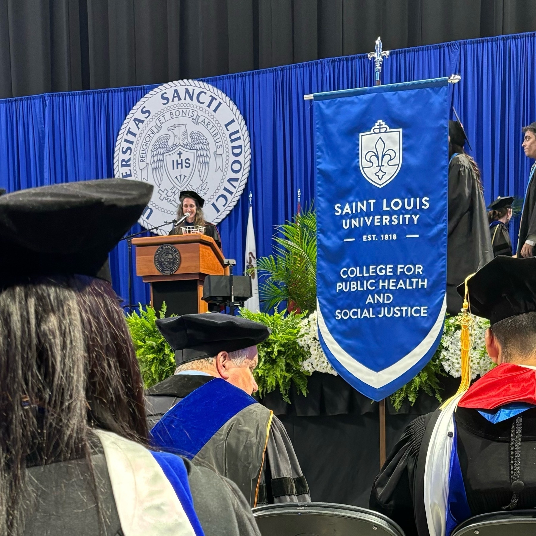 A photo of the pre-commencement ceremony at SLU, featuring the banner for the CPHSJ. 