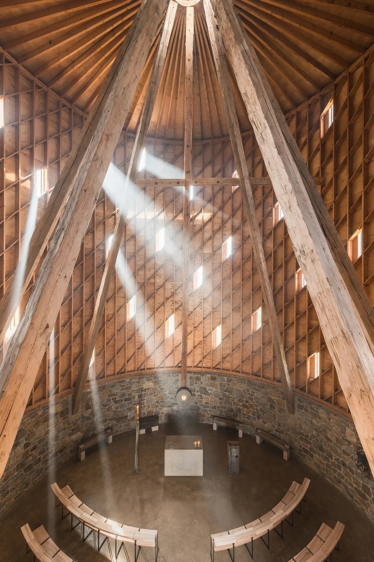 Wooden beams reaching to the roof of this circular chapel. &10;&10;Rows of chairs positioned in semi-circular formation surrounding a stone altar. &10;&10;Our Lady of Sorrows Chapel in Nesvačilka, South Moravia, by Studio RCNKSK&10;(Image credit: Ondřej Bouška)