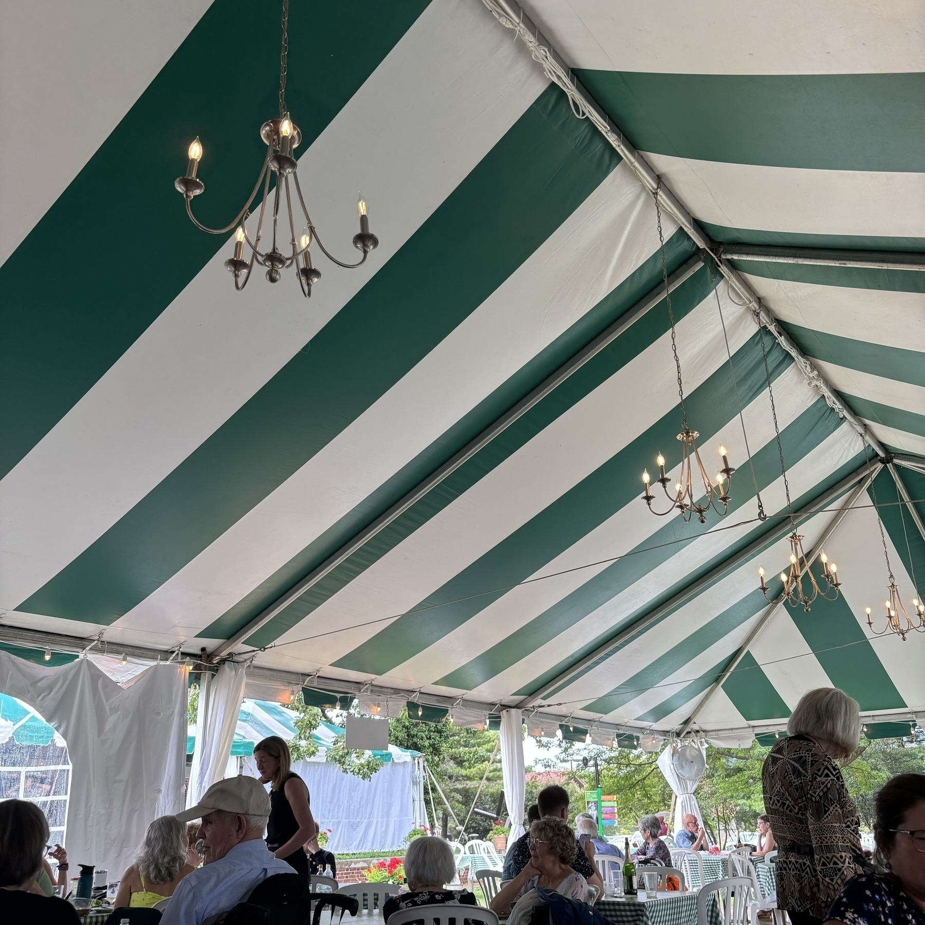A green and white striped tent, with four spindly chandeliers hanging in the center. 