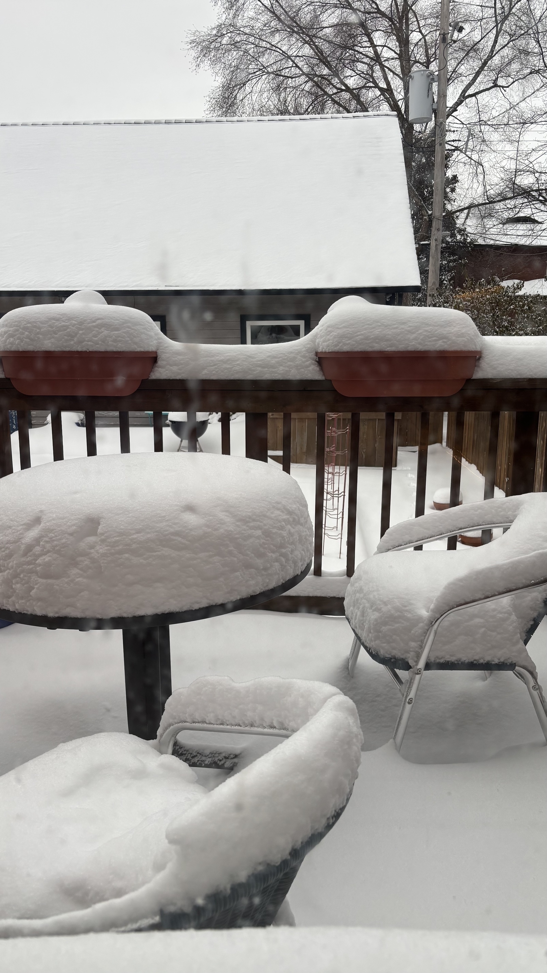 Two chairs and a small table on a deck, covered with white snow, about 8-10 inches deep