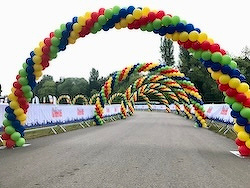 Colorful balloon arches line a pathway, creating a festive atmosphere against a backdrop of trees and banners.