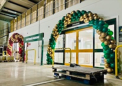 A brightly lit indoor space features two colorful balloon arches, one in green and gold, and the other in red and gold, framing entrances.