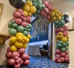 A colorful balloon arch with pink, green, and yellow balloons decorates a hallway entrance.