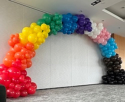 A colorful balloon arch arranged in a gradient across a room corner.