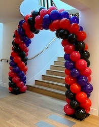 A colorful arch made of red, pink, purple, and black balloons stands at the base of a staircase.