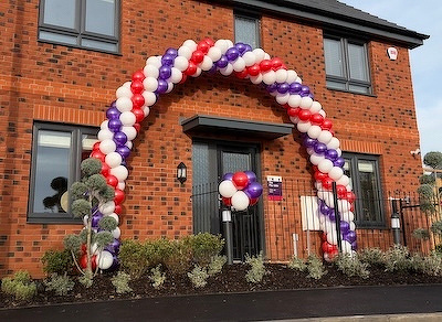 A festive arch made of red, white, and purple balloons decorates the entrance of a brick building.