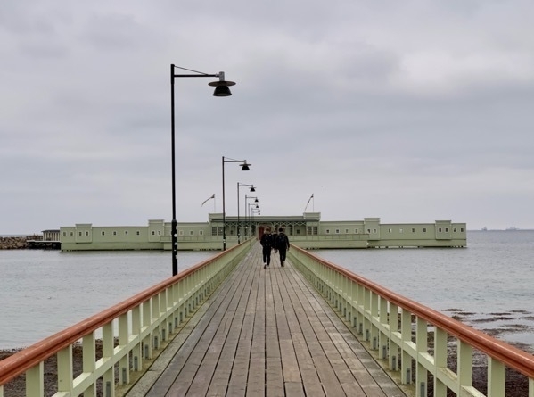 A few people walking along the pier leading to Ribersborgs Kallbadhus Open Air baths (Swedish sauna)