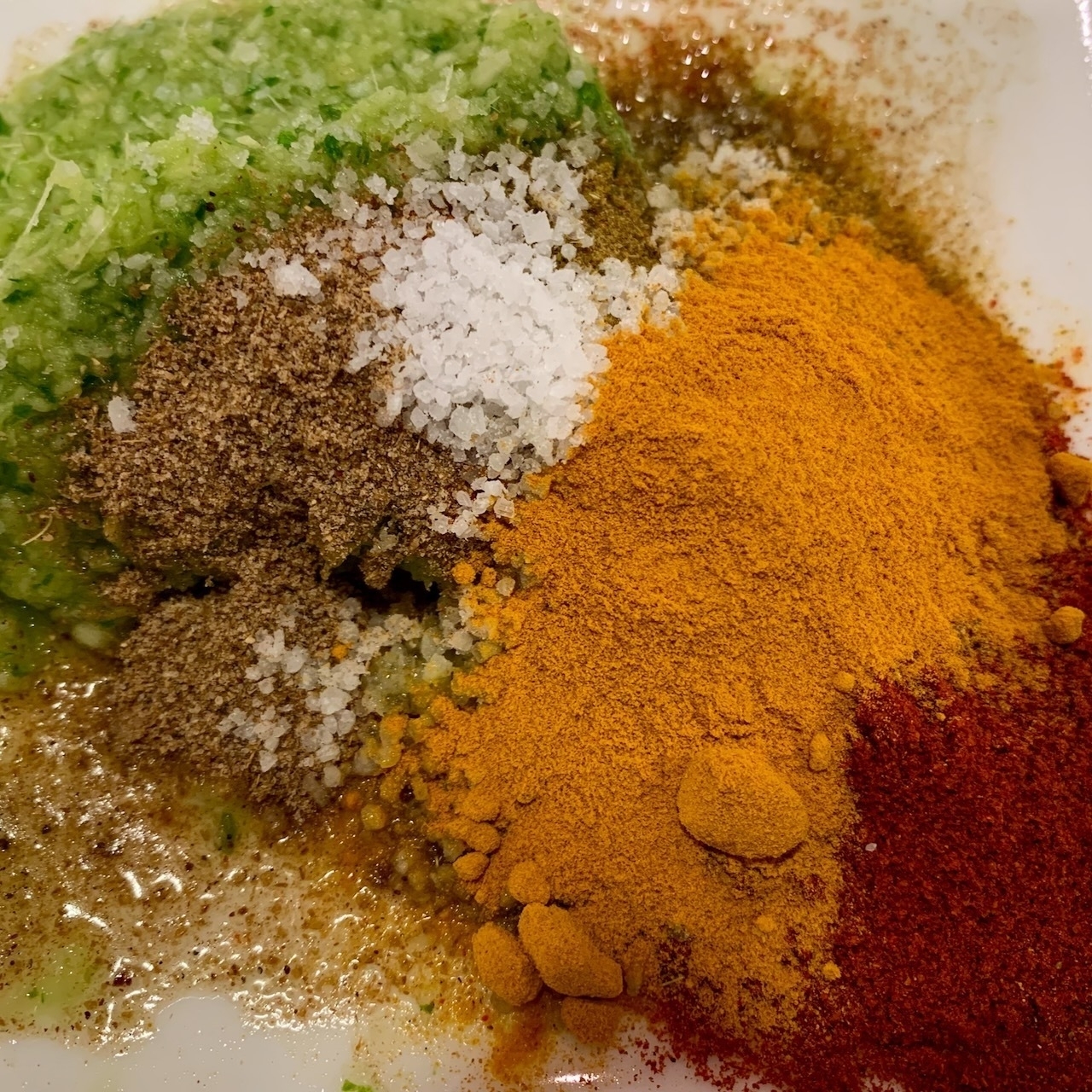 spices of various colours in a mixing bowl, comprising of ginger, garlic and coriander/cilantro paste (green), cumin & coriander (brown), paprika (red), turmeric (orange) and salt (white)