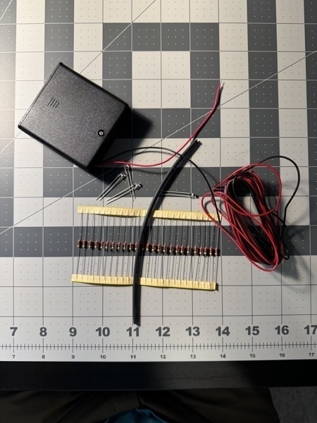 Pieces of the lighting kit that came with the flying dutchman model. Shown is a big black battery pack, some red and black wires, a bunch of LED lightbulbs, some resistors and some shrink tubing. 