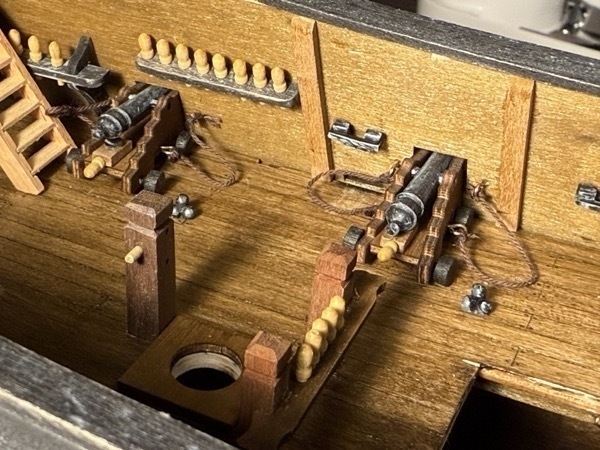 View of a couple of the cannons on the main deck of the flying dutchman model ship with a couple of piles of cannon balls next to them. Also shown are some belaying pin rails. 