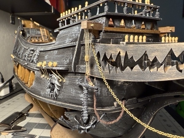 View of the prow of the flying dutchman model ship showing one of the anchors mounted and hanging down from its support. Also shown are some brass chains used to hold the figurehead in place. 