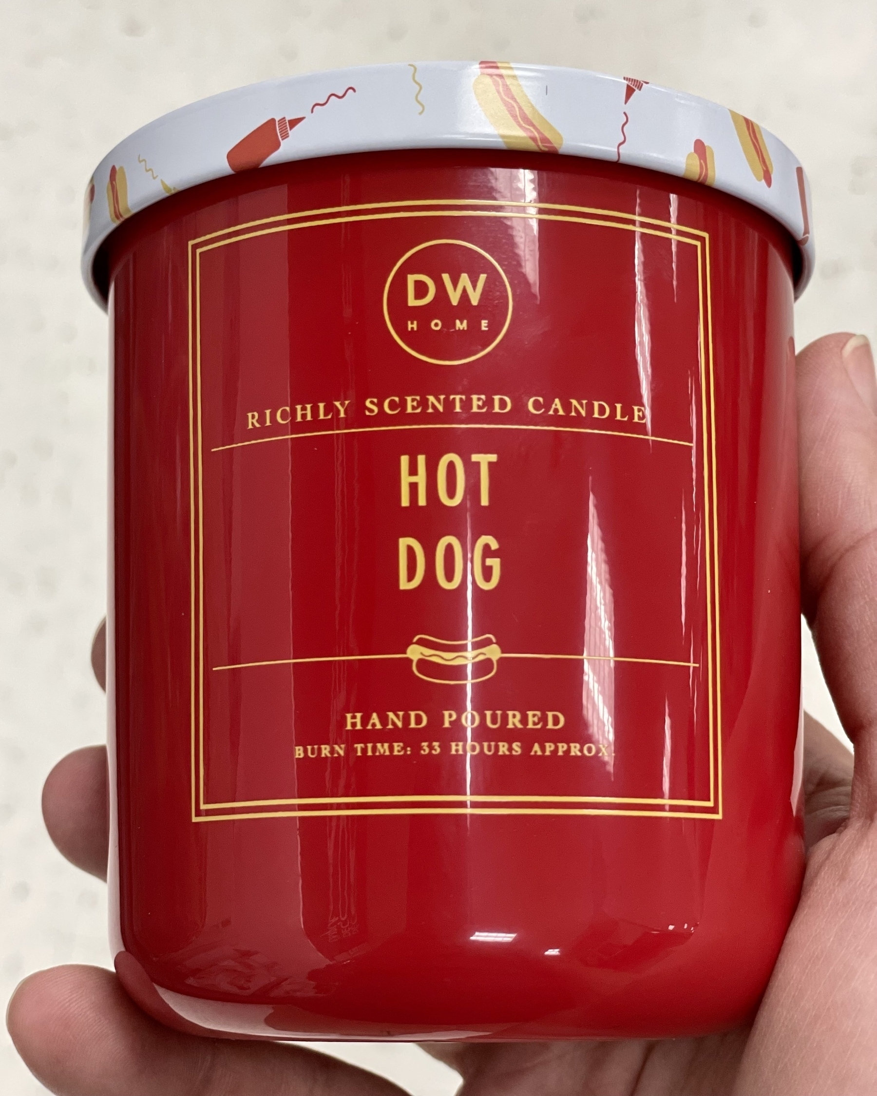 A photo of a scented candle in a red glass jar. The fragrance, "hot dog," is proudly printed on the jar.