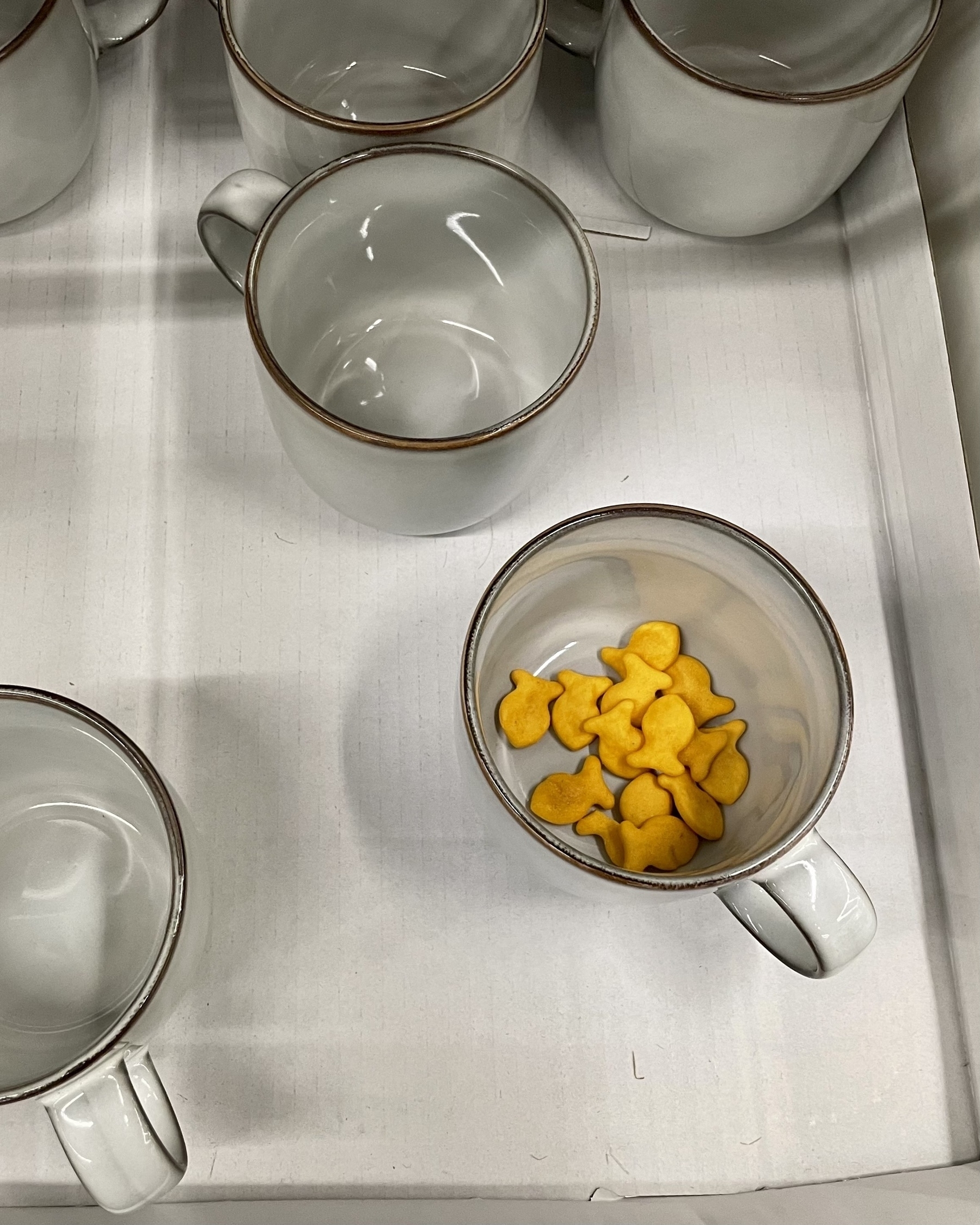 A top-down photo of some mugs on display at IKEA, one of which as a small pile of goldfish crackers in it.