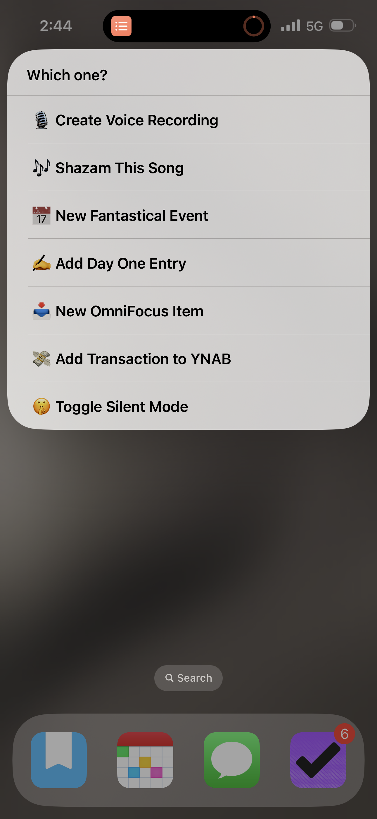 A screenshot of an iPhone Home Screen showing a menu of shortcuts to run, including creating a voice recording, Shazam, and creating an entry in OmniFocus, Fantastical, Day One, or YNAB, or toggling Silent Mode.