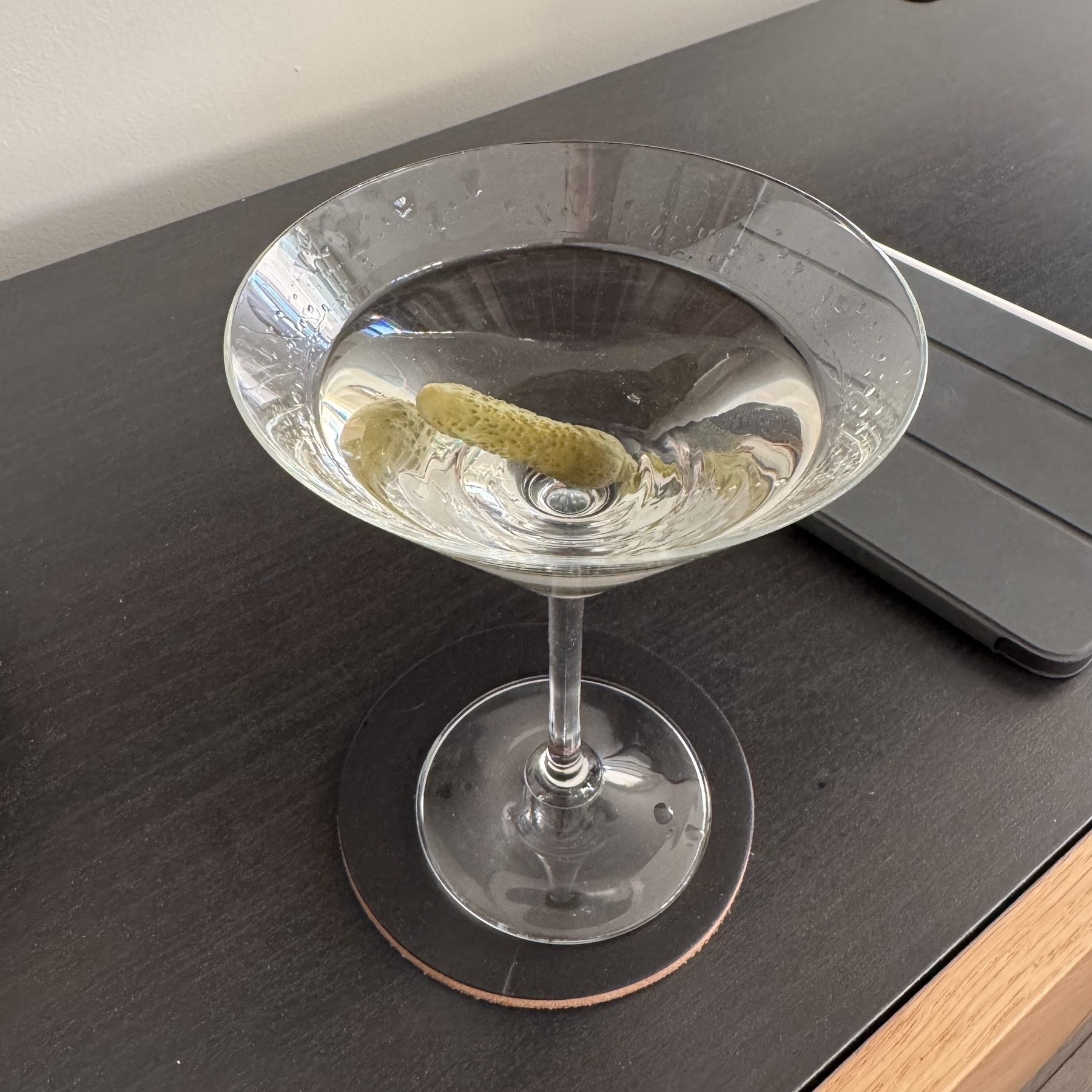 A martini cocktail sits on furniture. A small cornichon garnishes the drink.