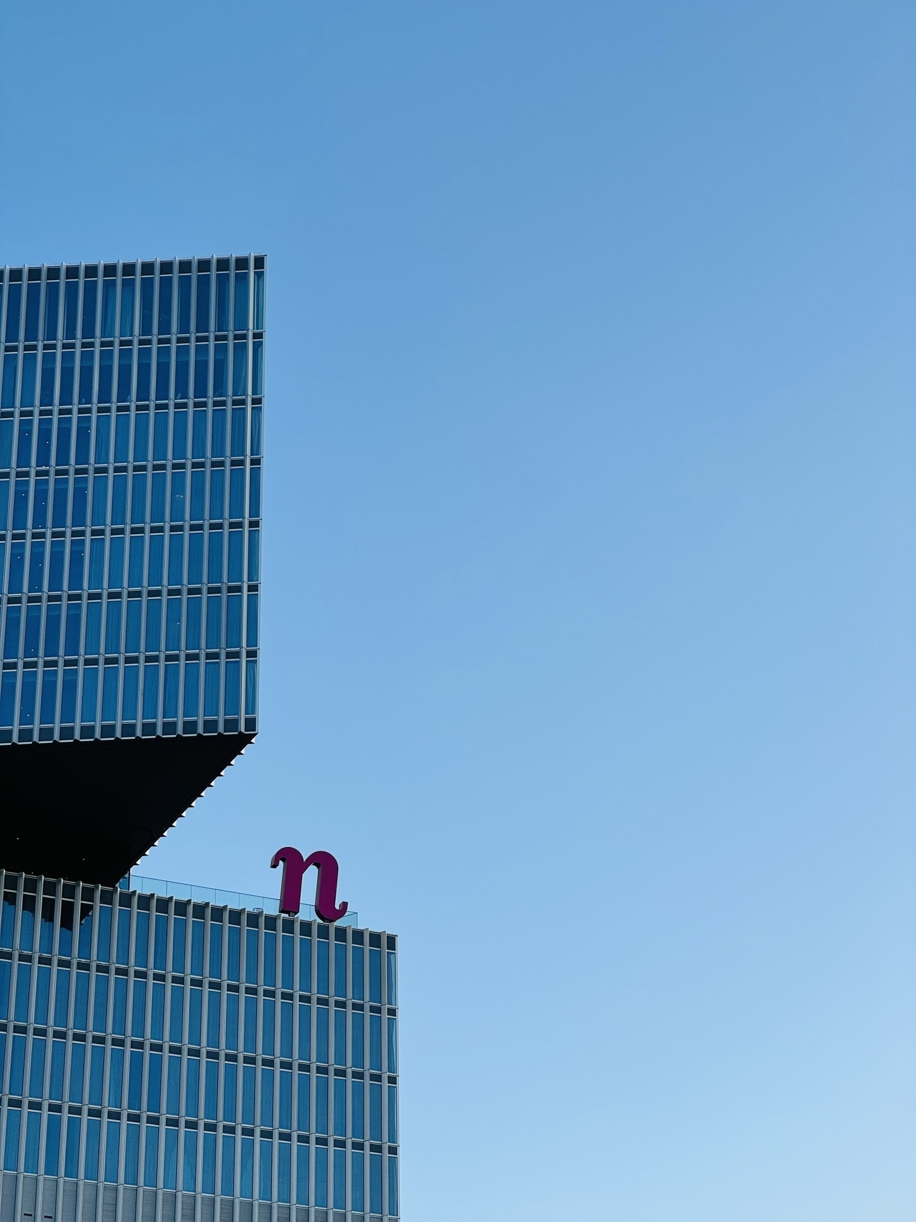 A pointy glass building with a “n” sign on it, against a clear blue sky.