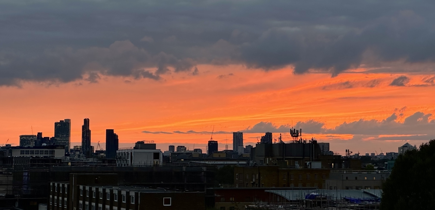A band of orange sky at sunset, sandwiched between a building filled horizon below and grey clouds above.