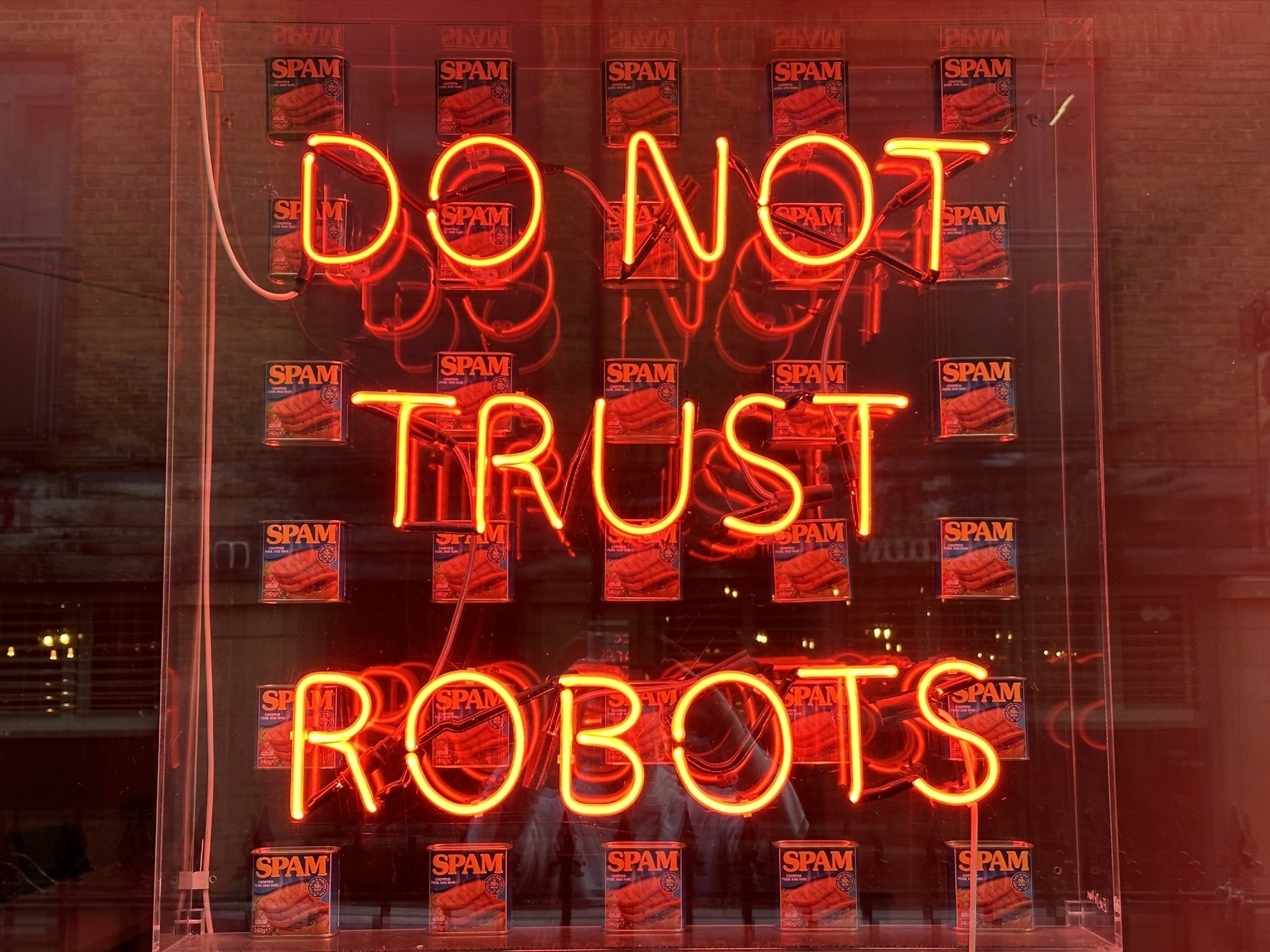 A red neon sign that says DO NOT TRUST ROBOTS, overlaid on a grid of 30 cans of SPAM luncheon meat.