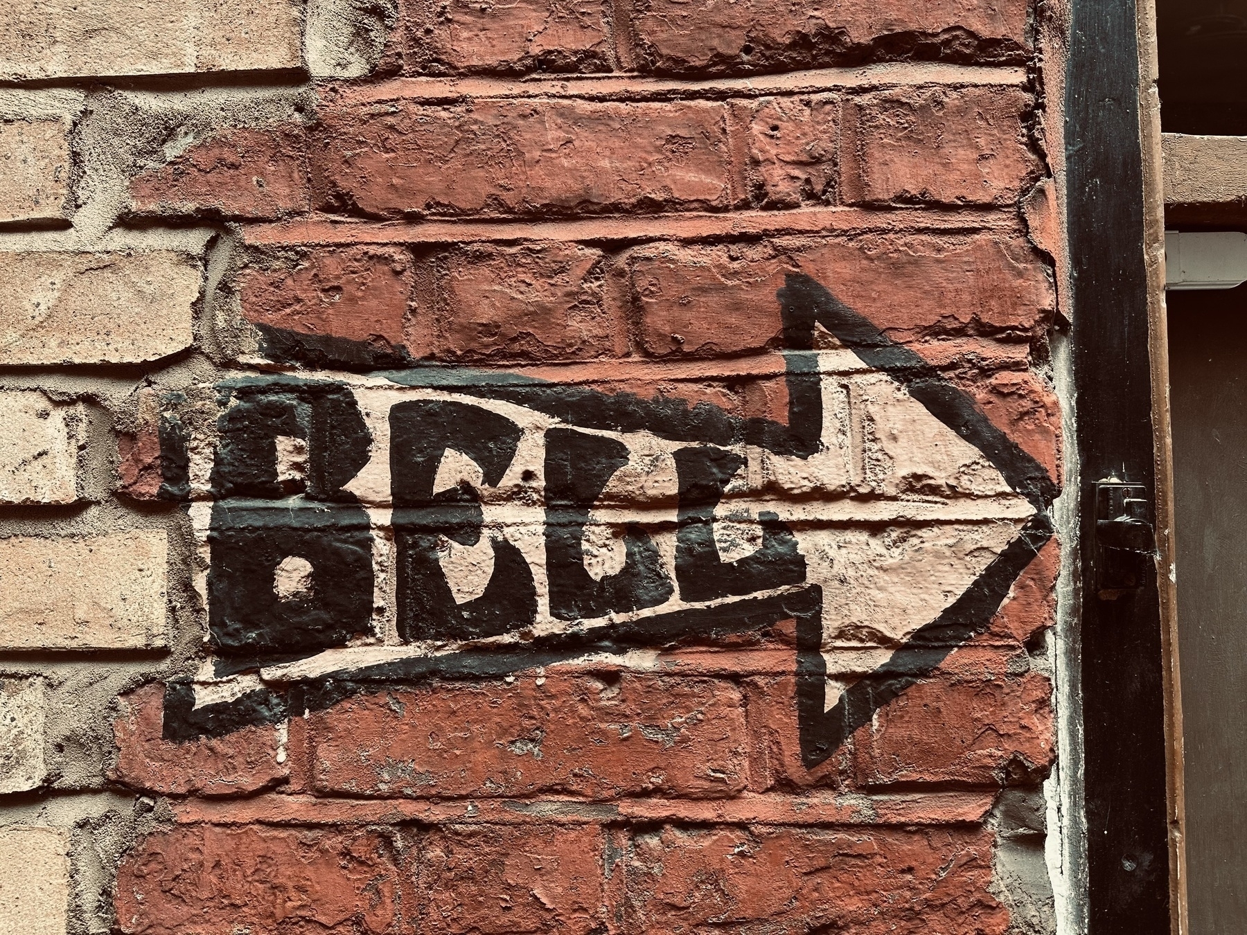 A white arrow with the word Bell in it painted on to a brick wall that’s painted red. The arrow points to a taped over doorbell.
