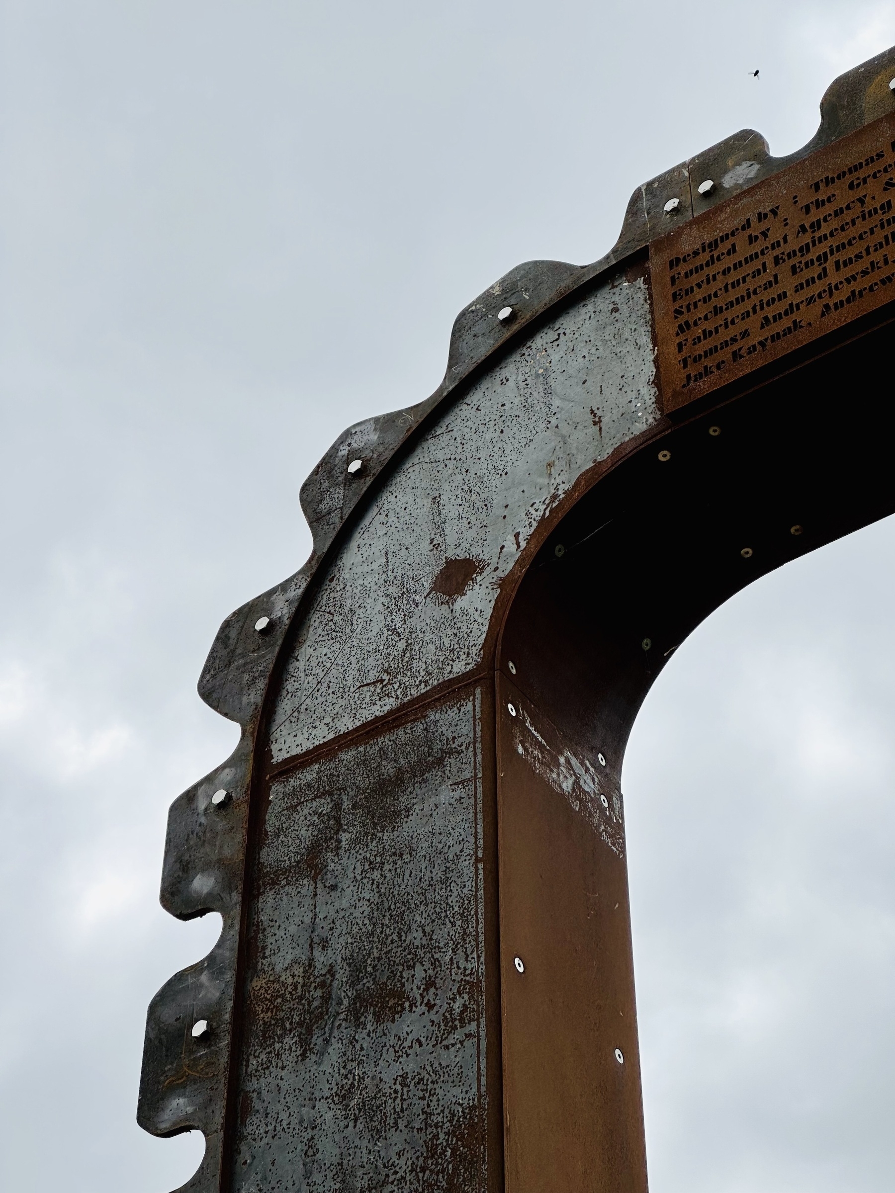 The corner of a toothed metal frame. The metal is partially rusted, making patterns of grey and orange.